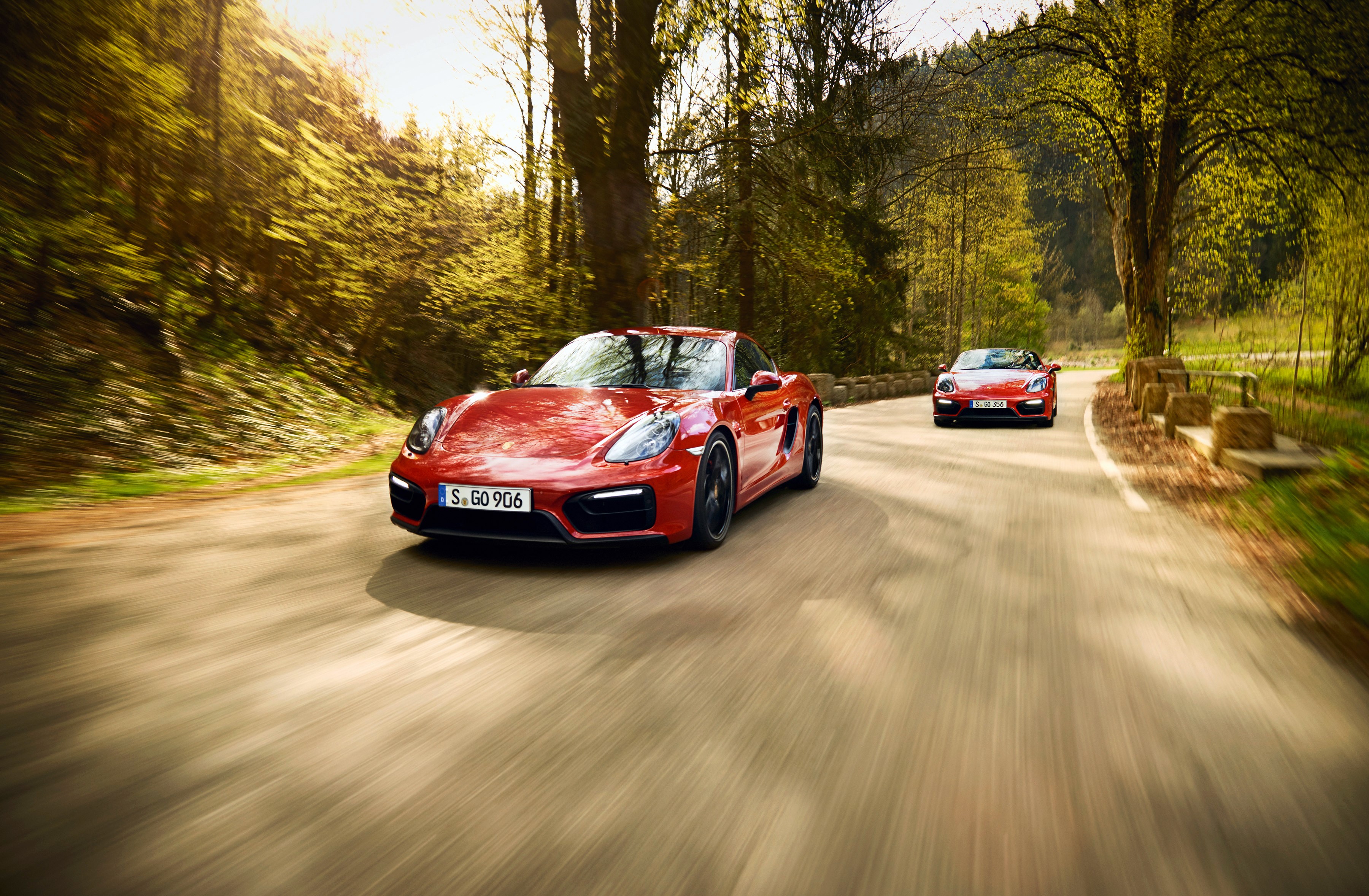 Two red Porsche cars driving on a forest road HD Wallpaper