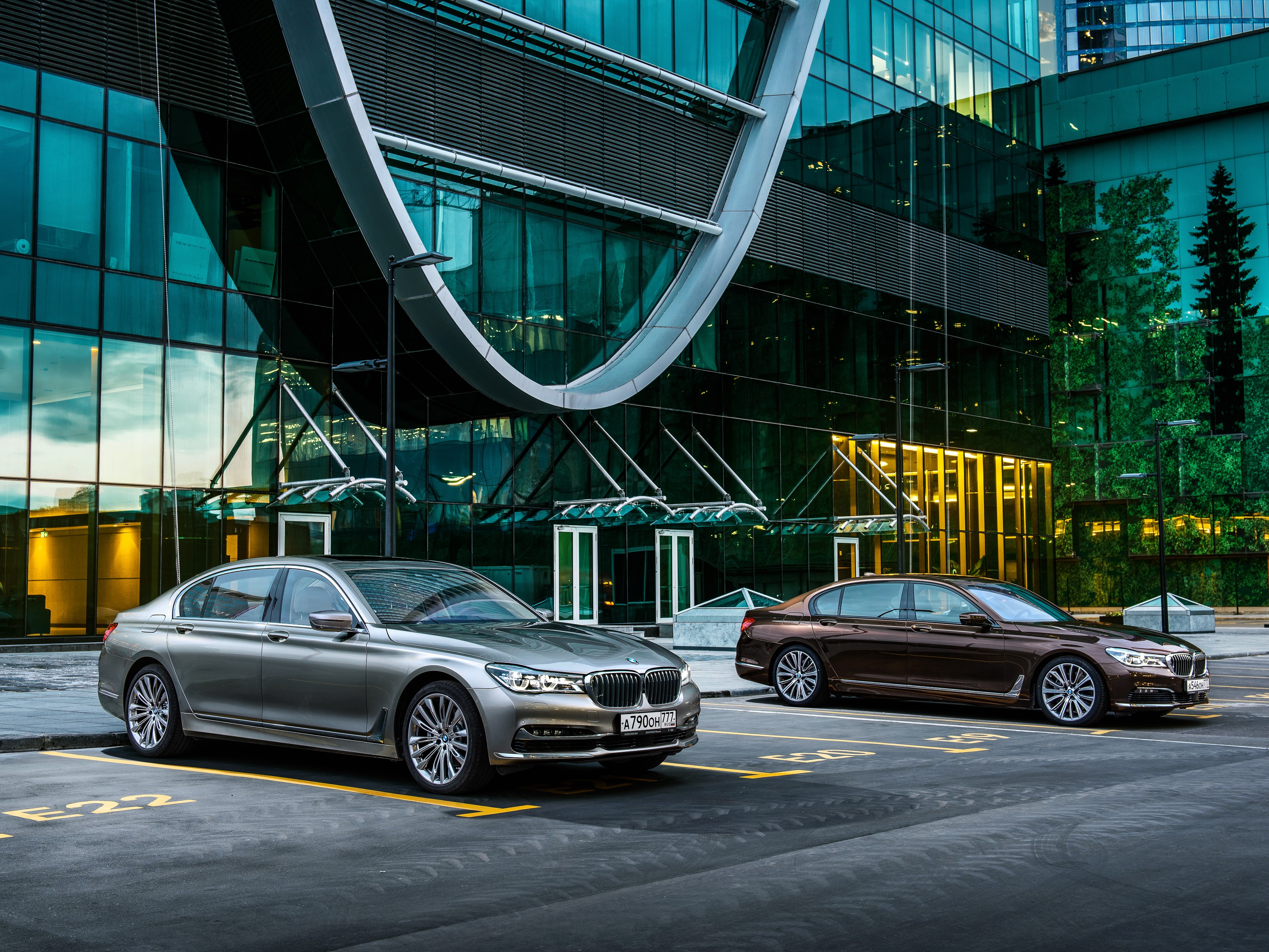 Two BMW 7-Series G12 cars parked in front of a modern building HD Wallpaper