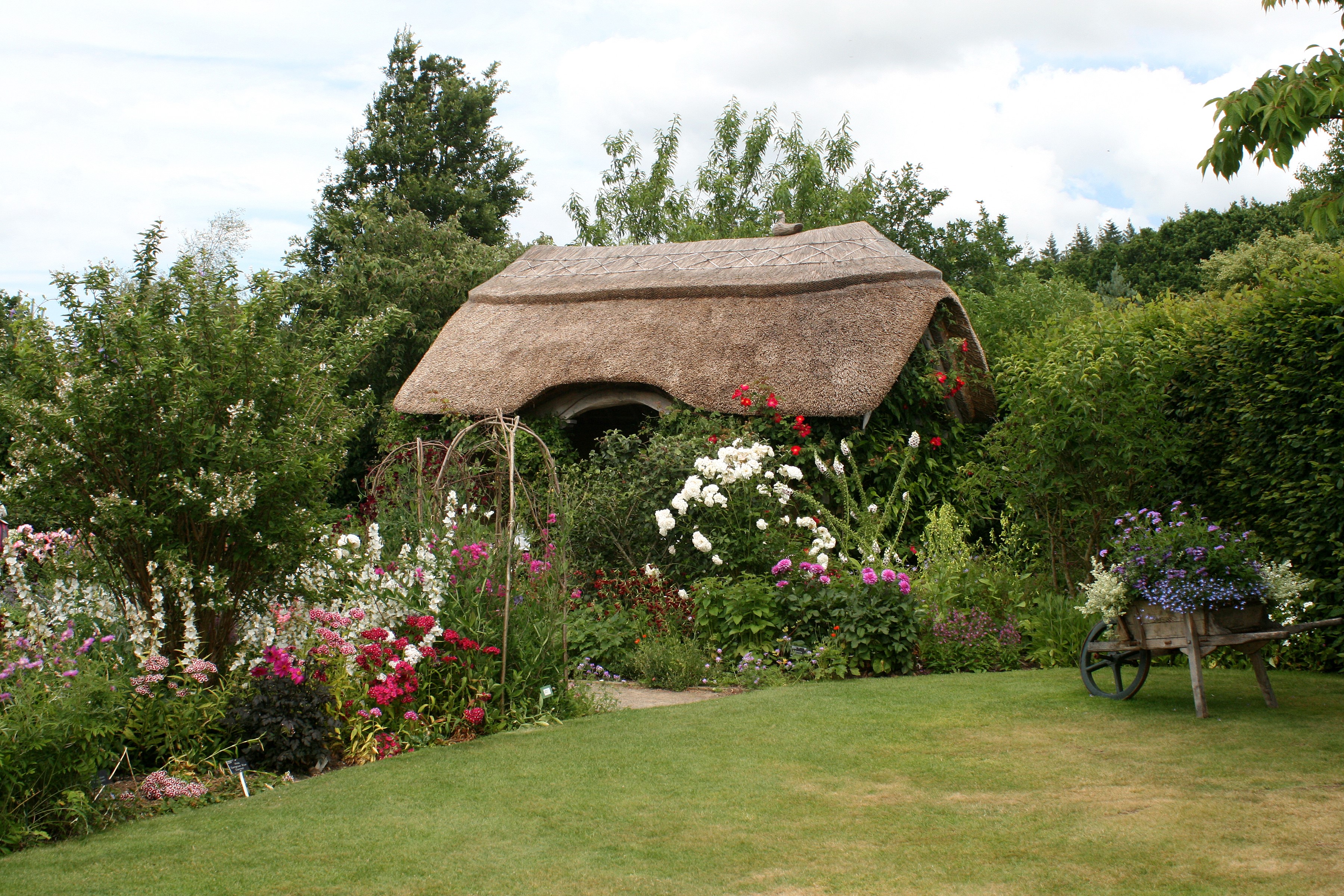Thatched cottage garden with flowers and wheelbarrow HD Wallpaper
