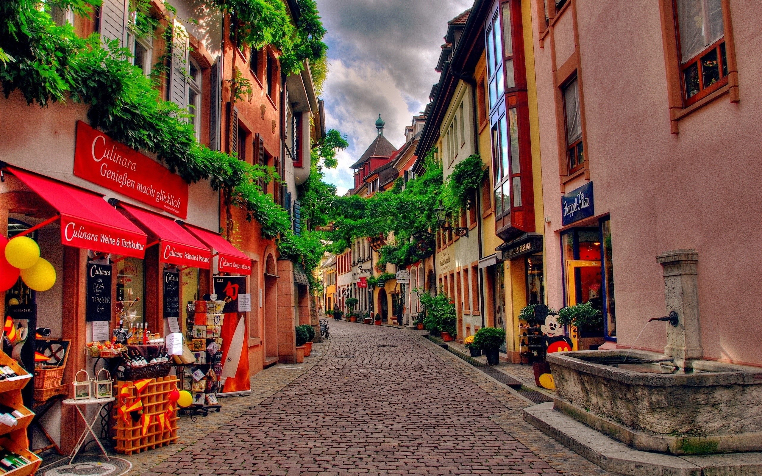 Cobblestone street with shops and fountain HD Wallpaper