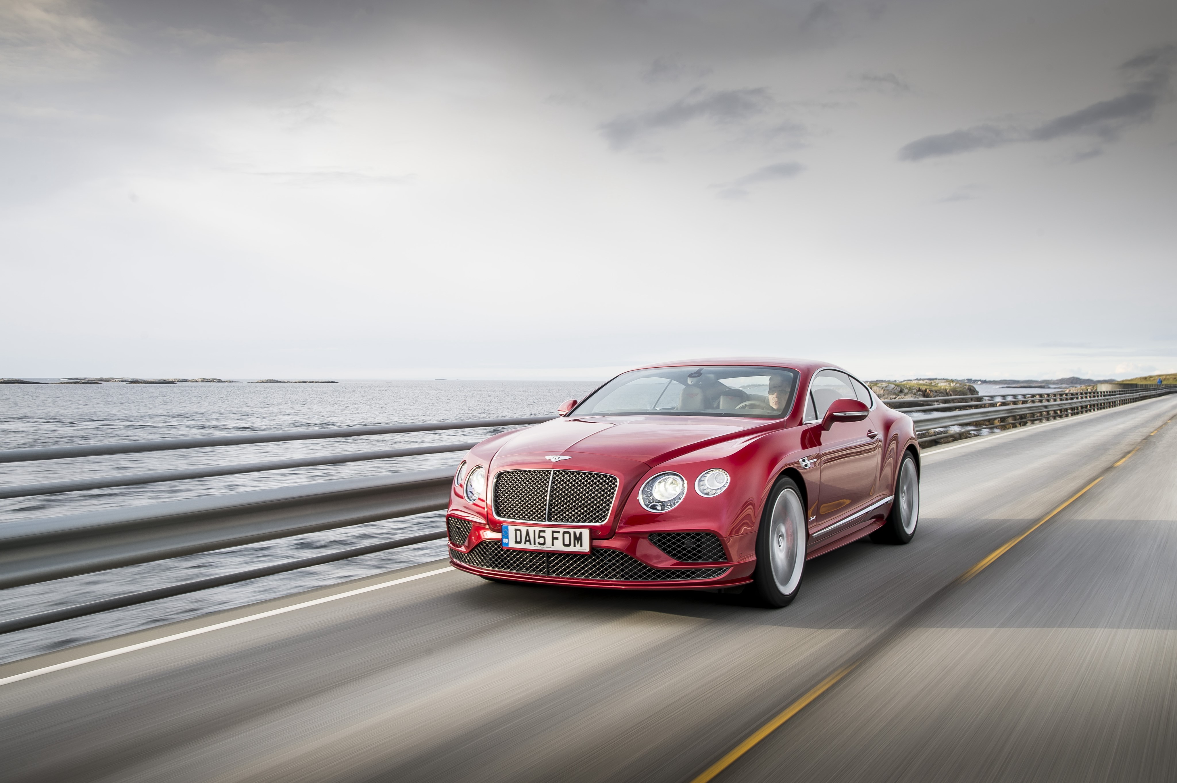 Red Bentley Continental GT driving on a coastal road HD Wallpaper