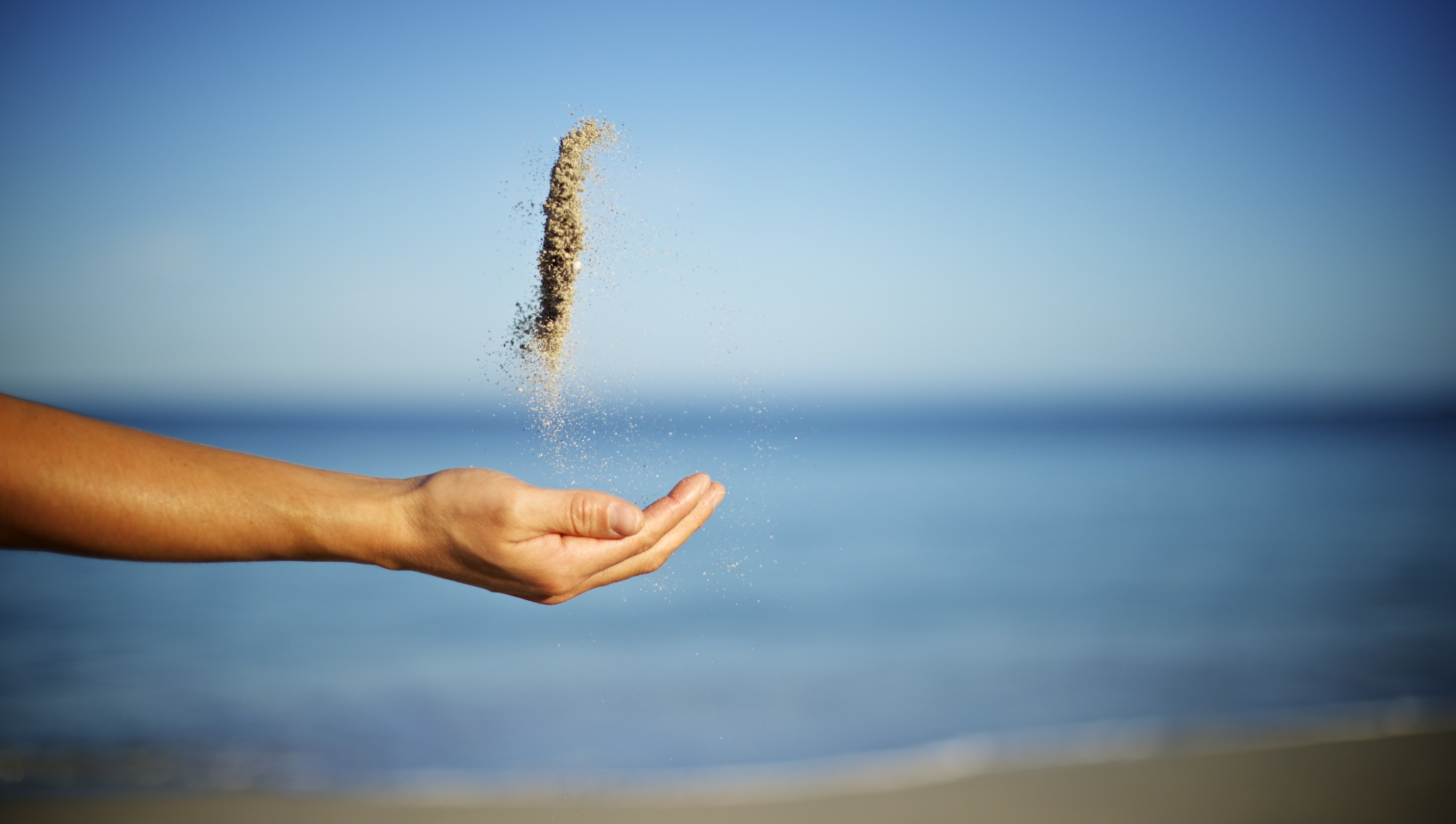 Hand pouring sand into the ocean HD Wallpaper