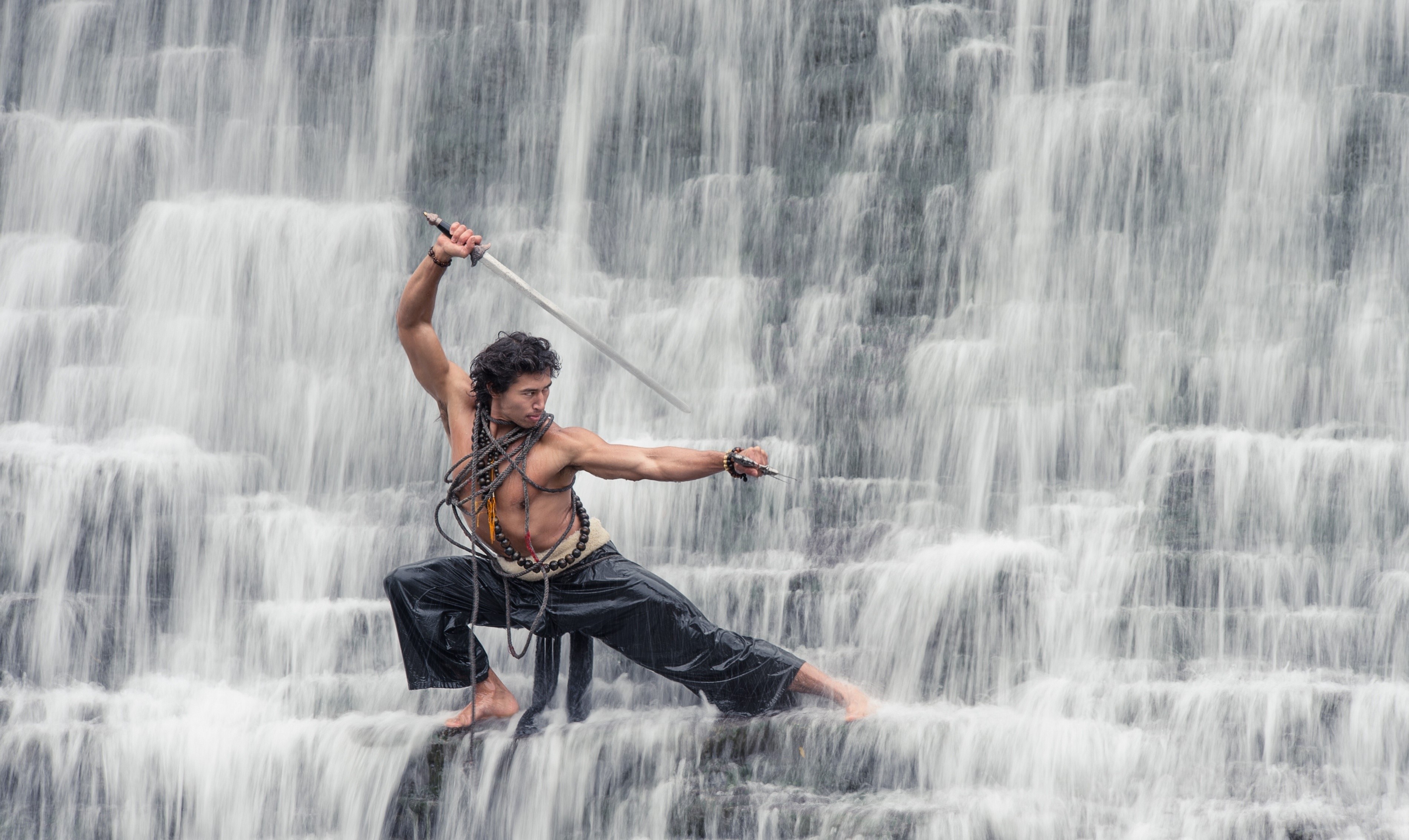 Man with sword in front of a waterfall HD Wallpaper