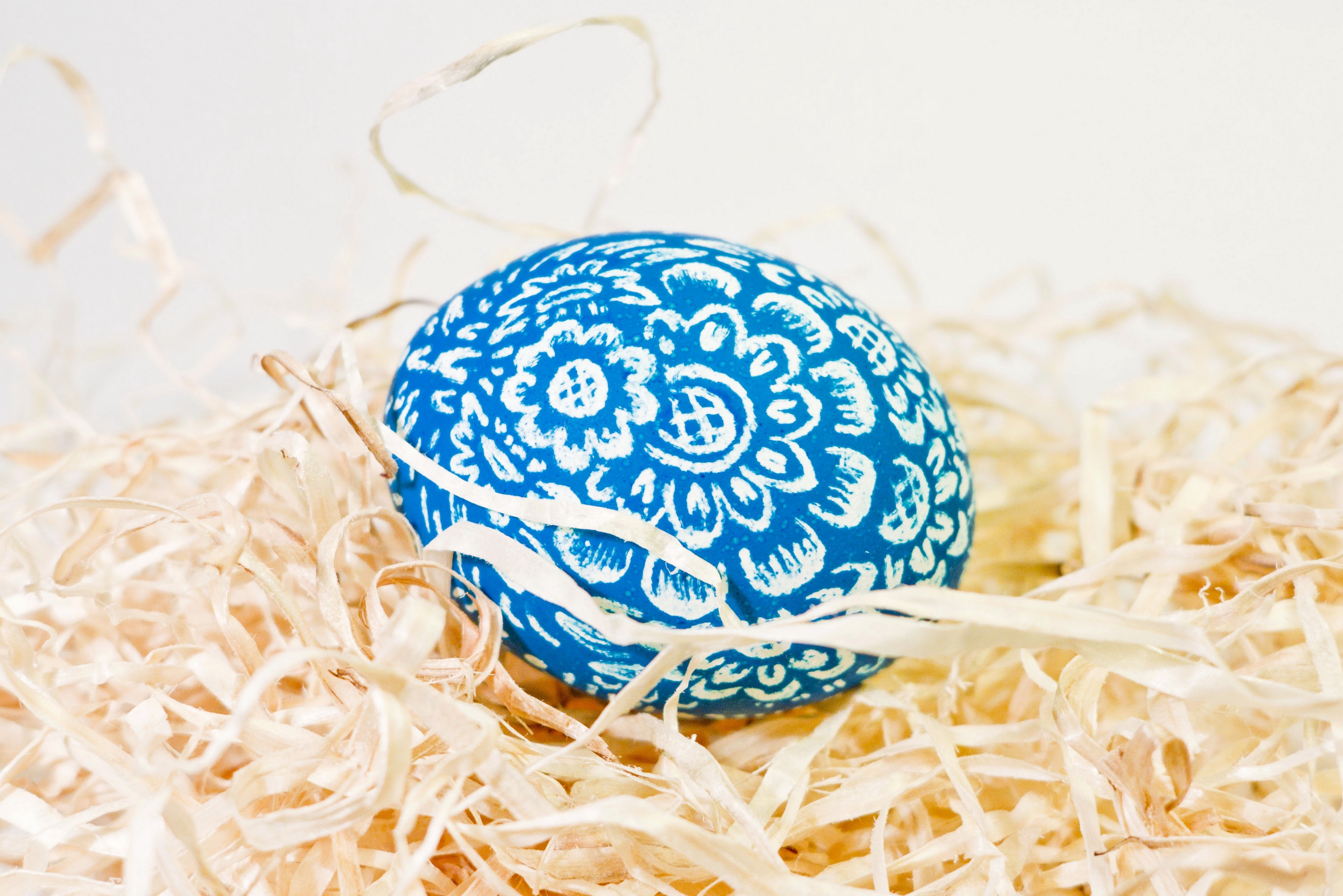 Blue Easter egg with white floral pattern in straw HD Wallpaper