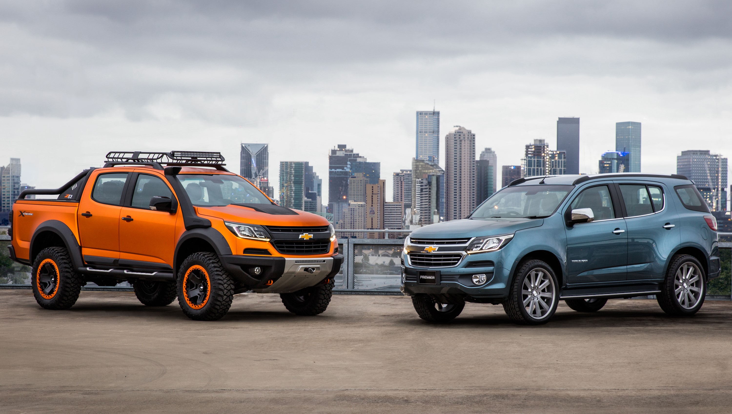 Two Chevrolet vehicles parked with city skyline HD Wallpaper