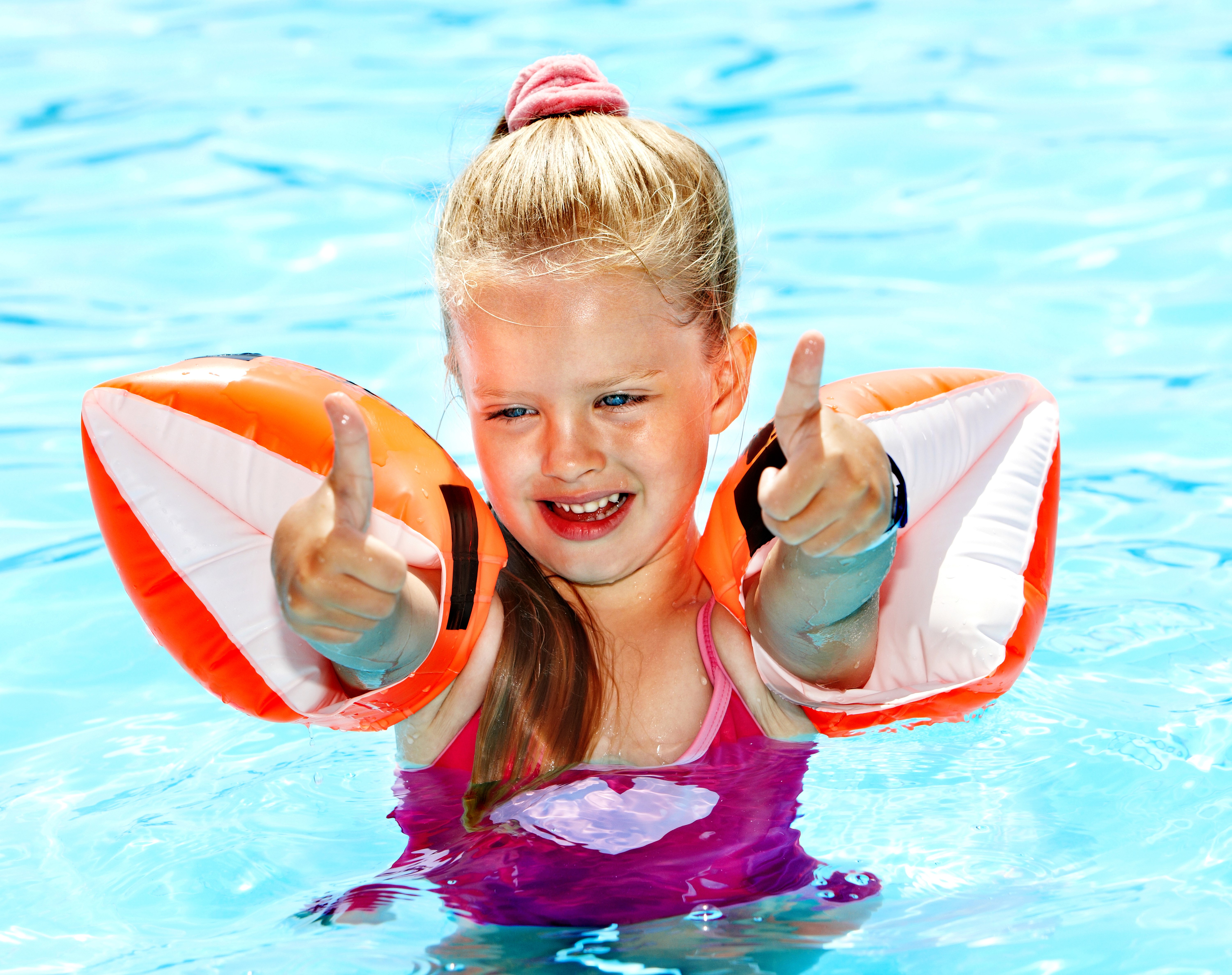 Little girl in pool with arm floaties giving thumbs up HD Wallpaper