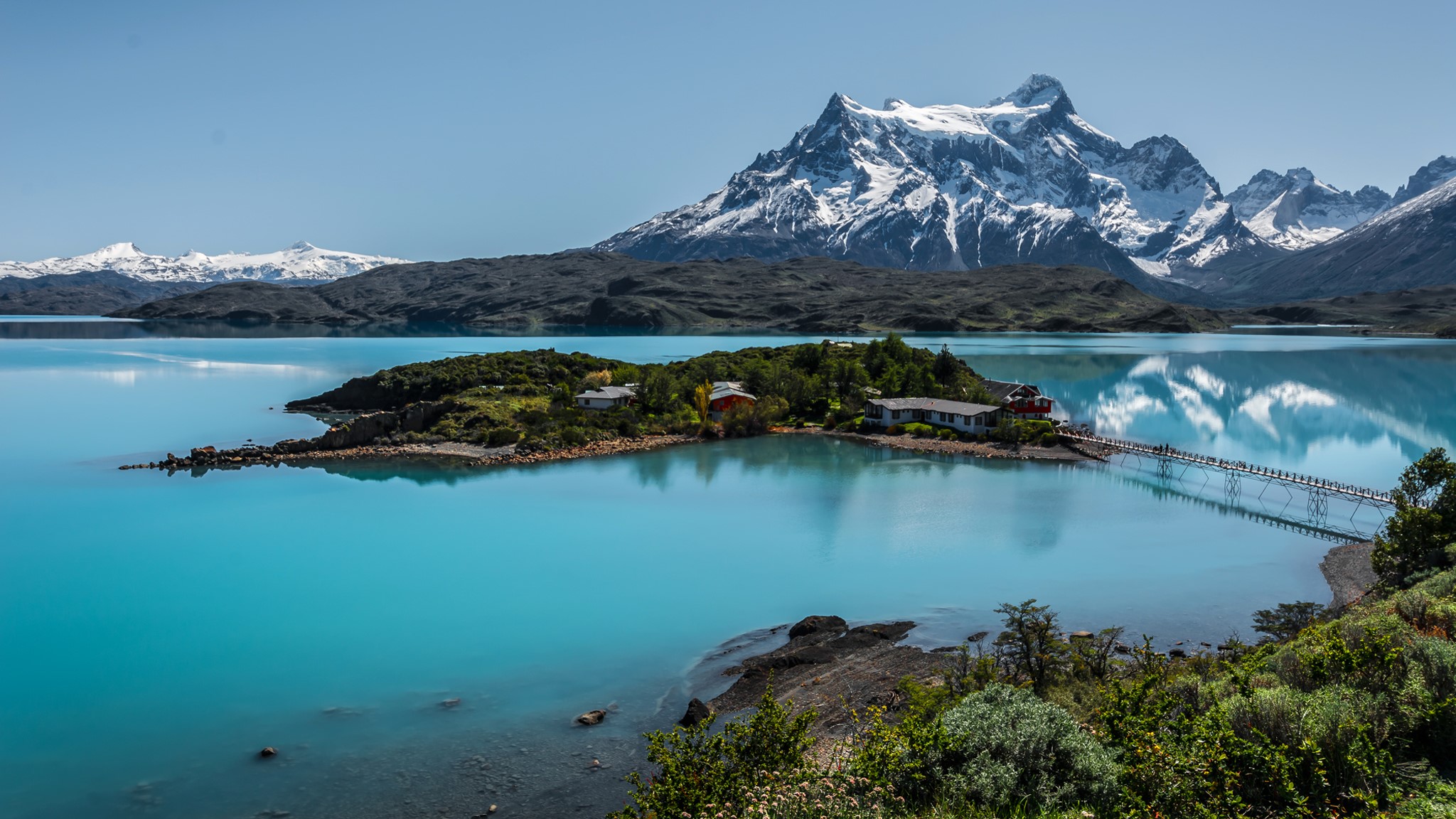 Island with buildings on a turquoise lake with snowy mountains HD Wallpaper