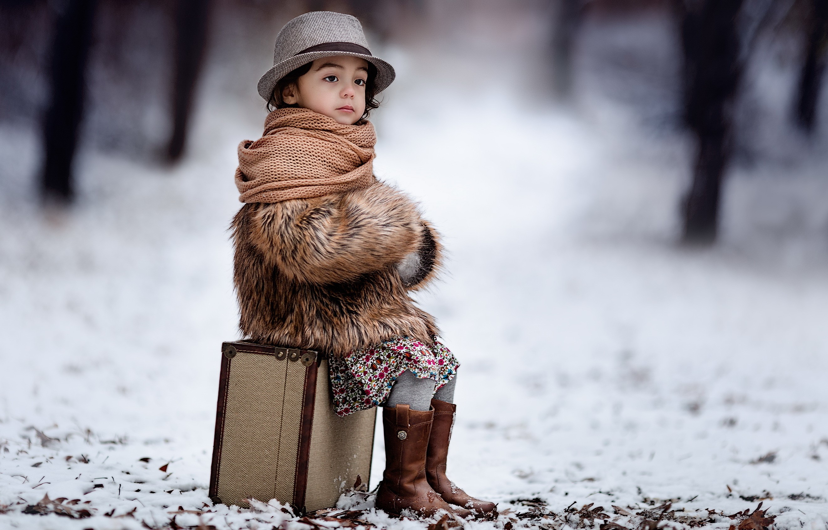 Girl in winter coat and hat sitting on suitcase in snow HD Wallpaper