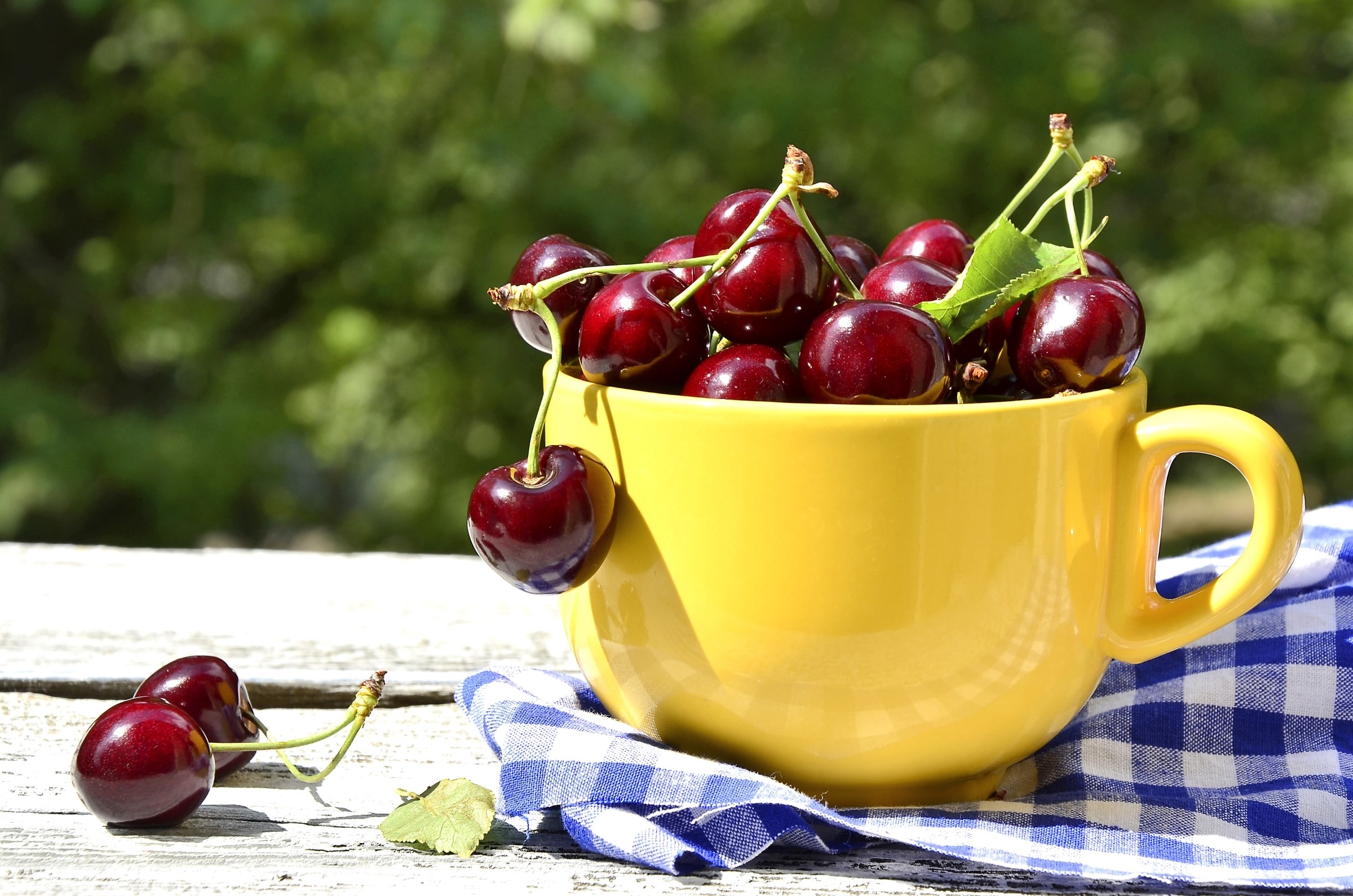Cherries in a yellow cup on a table HD Wallpaper