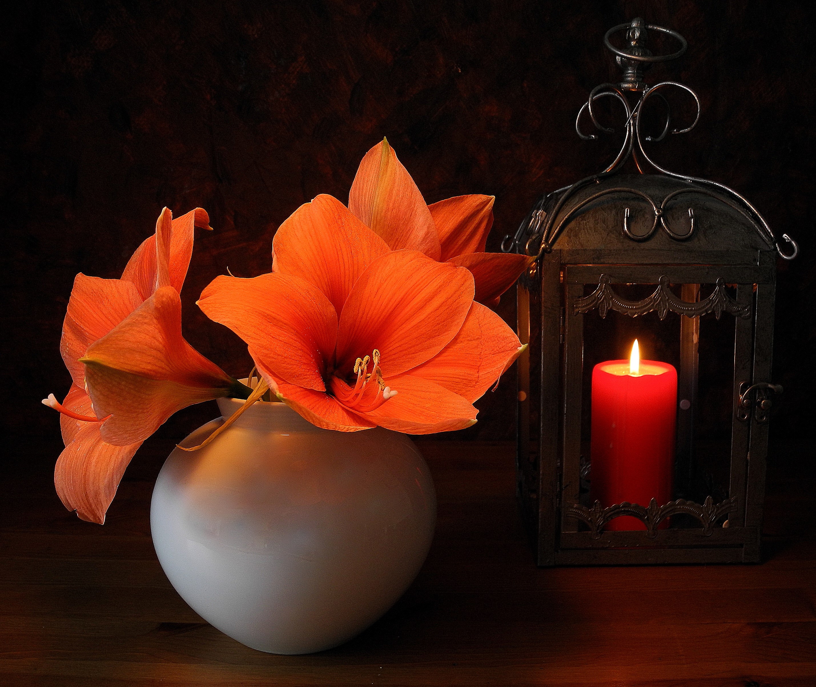 Orange lilies in a white vase next to a lit candle in a lantern HD Wallpaper