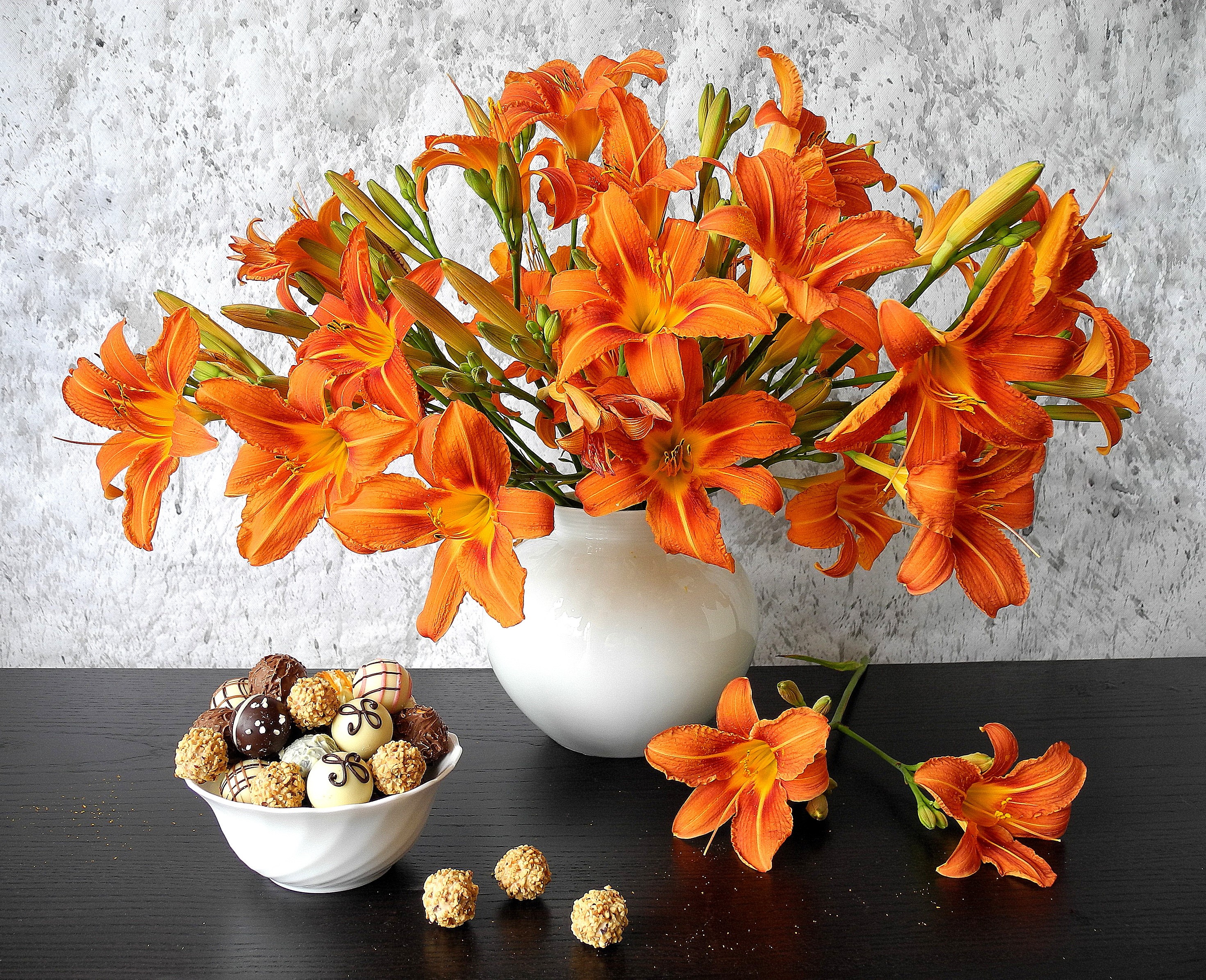 Orange lilies in a vase with a bowl of chocolates HD Wallpaper