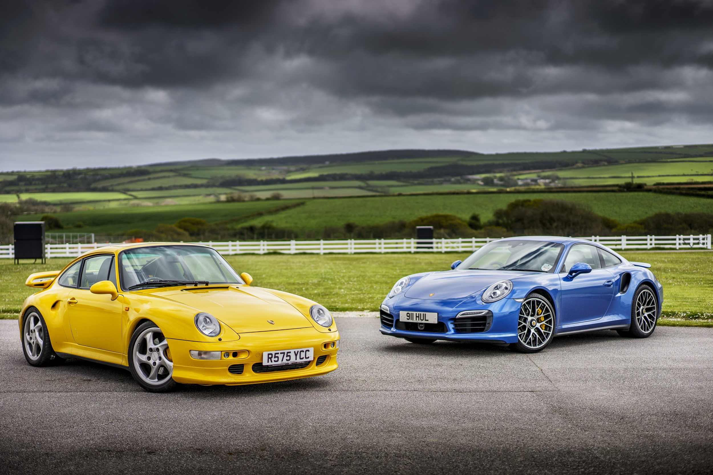 Two Porsche 911s, Yellow and Blue, on a Track HD Wallpaper