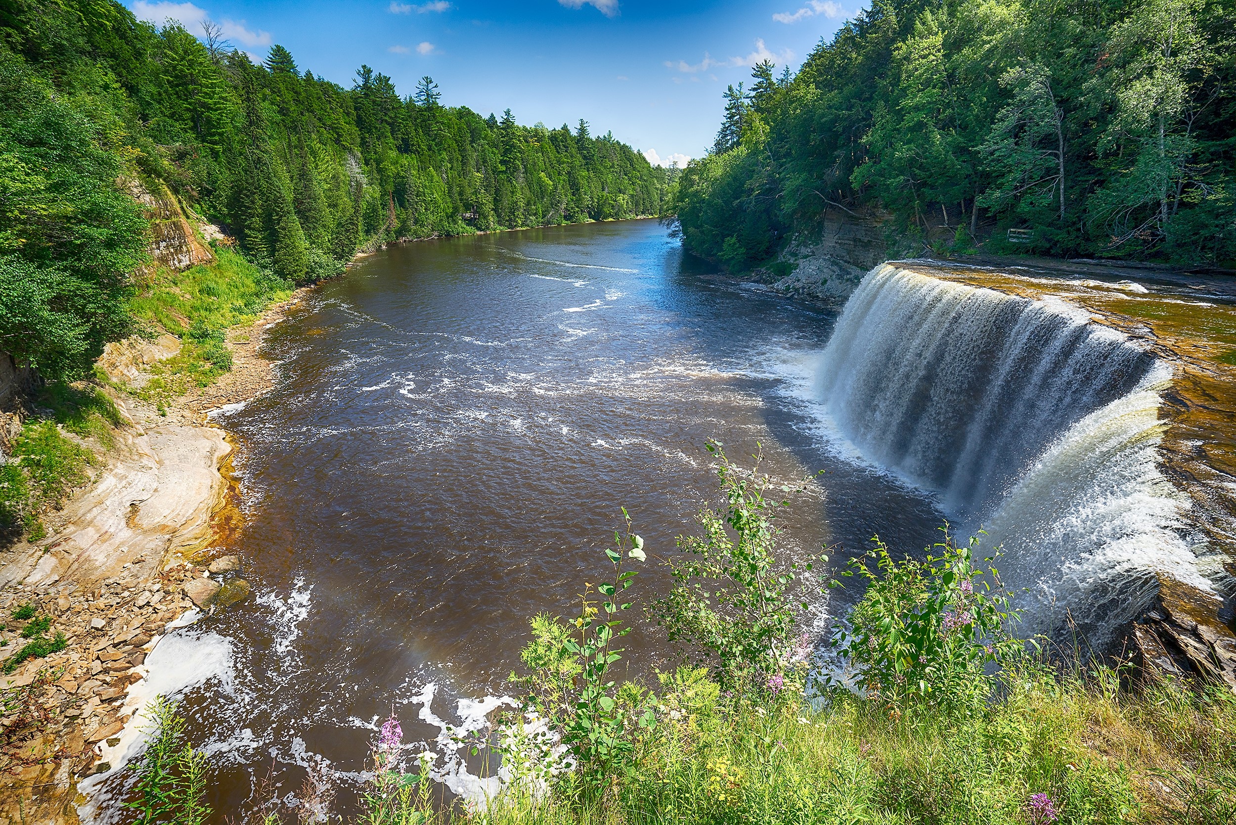 Waterfall in a lush green forest with a river HD Wallpaper
