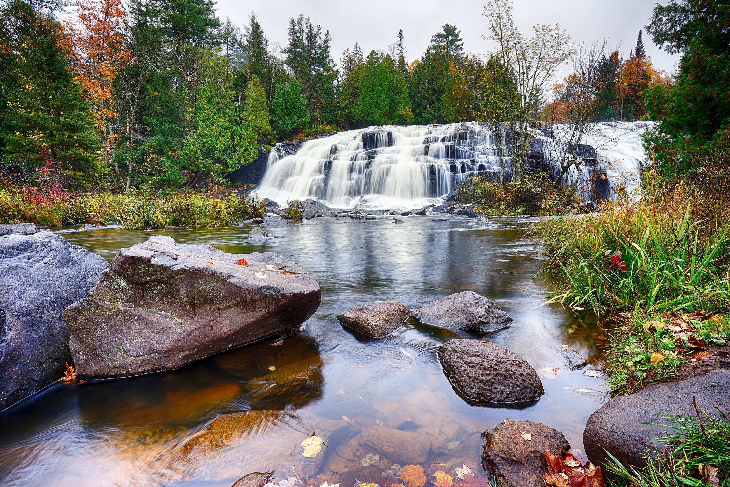 Waterfall cascading over rocks with autumn trees and river HD Wallpaper