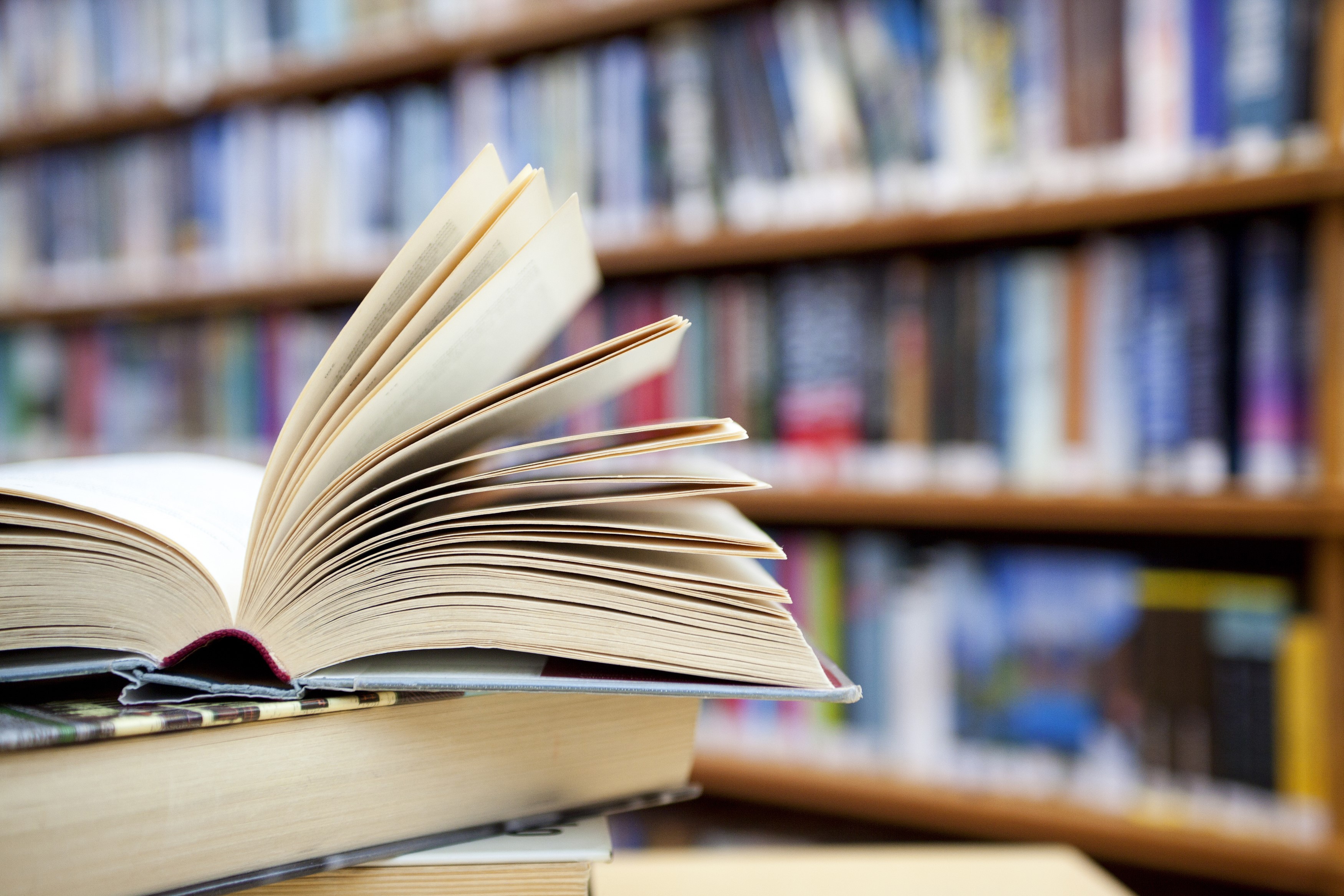 Open book on a stack of books in a library HD Wallpaper