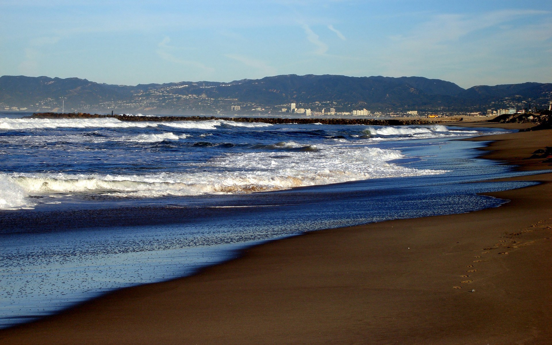 Waves crash on a beach with mountains in the background HD Wallpaper