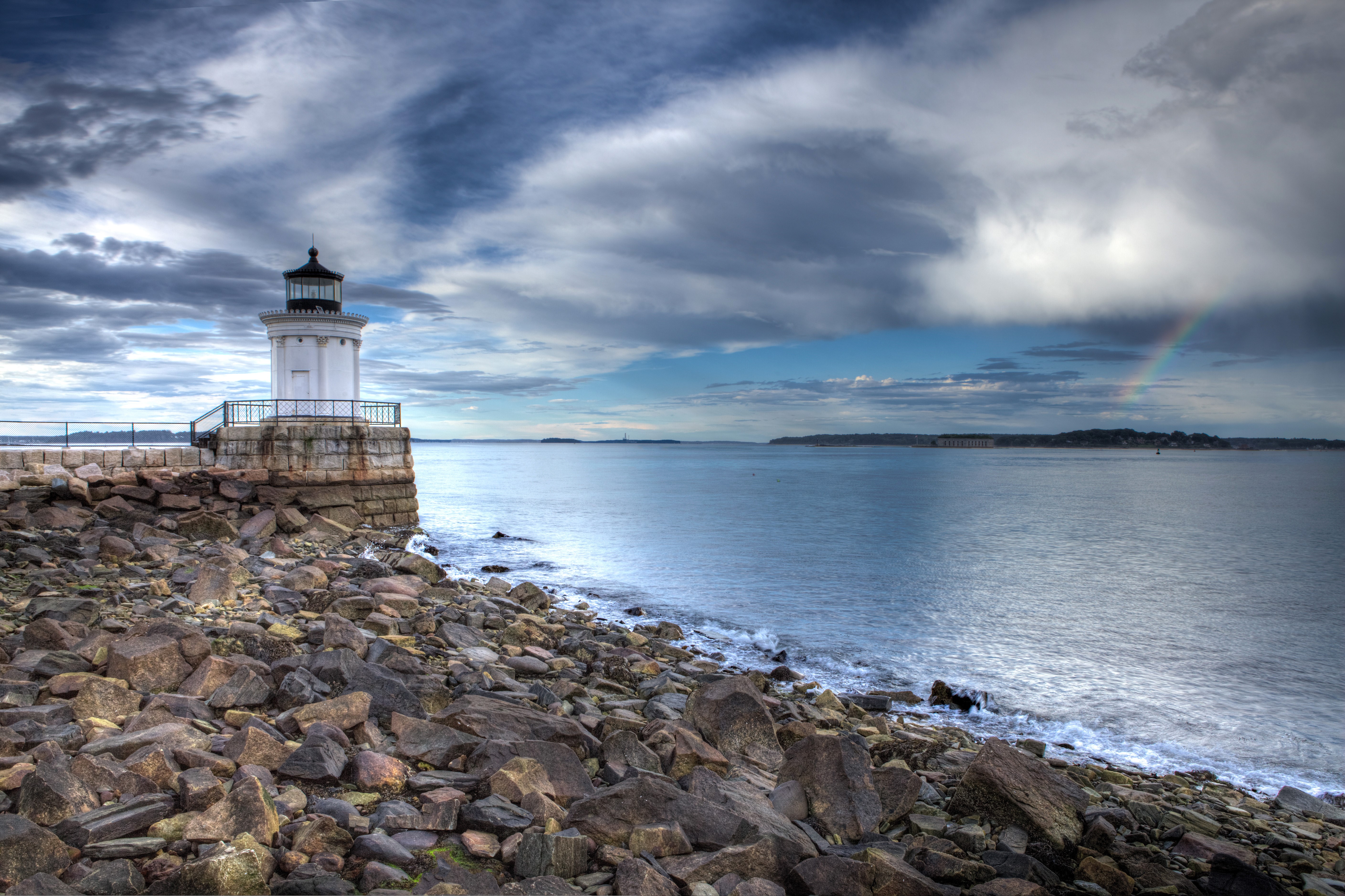 Lighthouse on a rocky coast with a rainbow HD Wallpaper