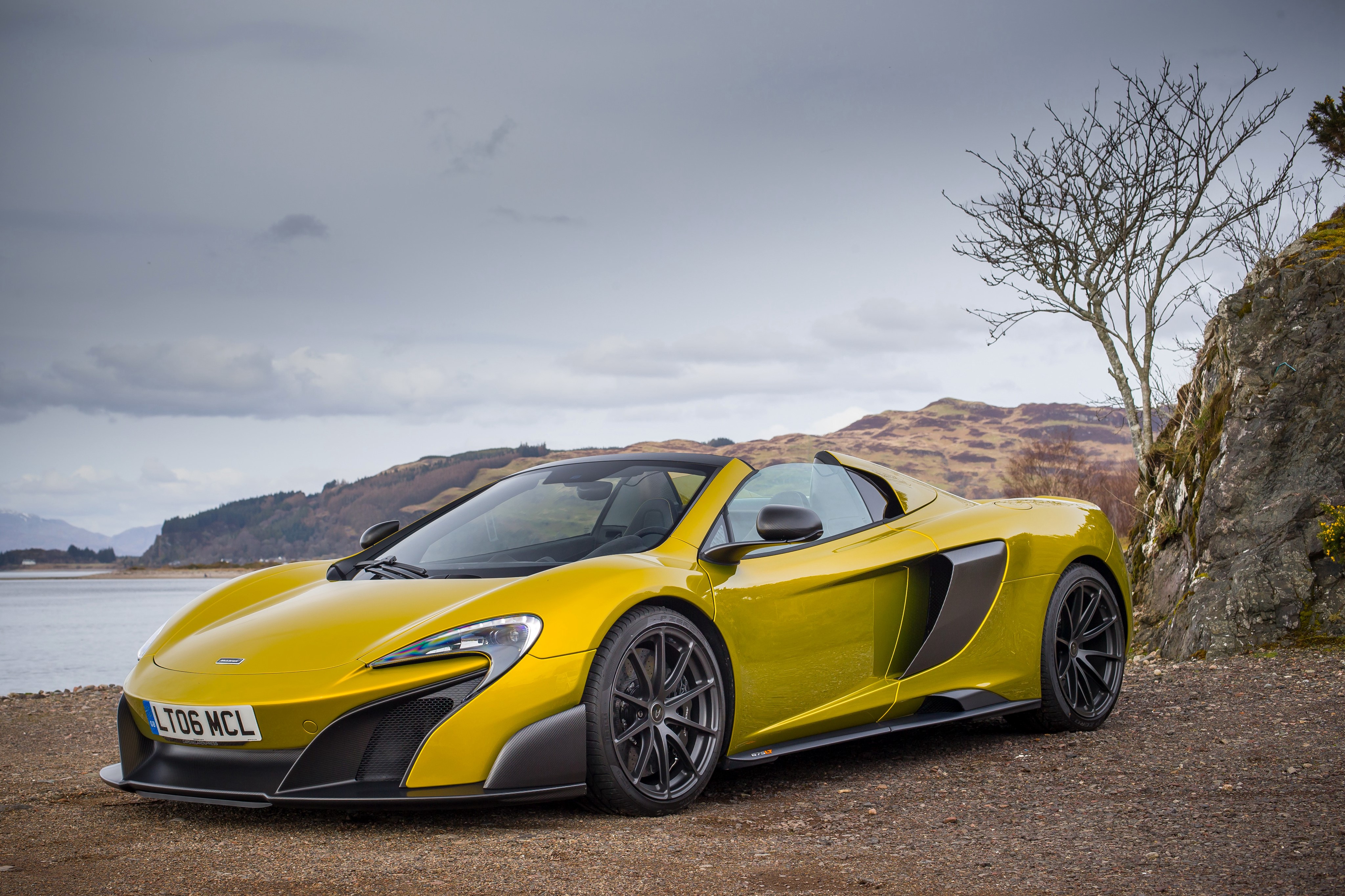 Yellow McLaren 675LT Spider parked by a rocky shore HD Wallpaper