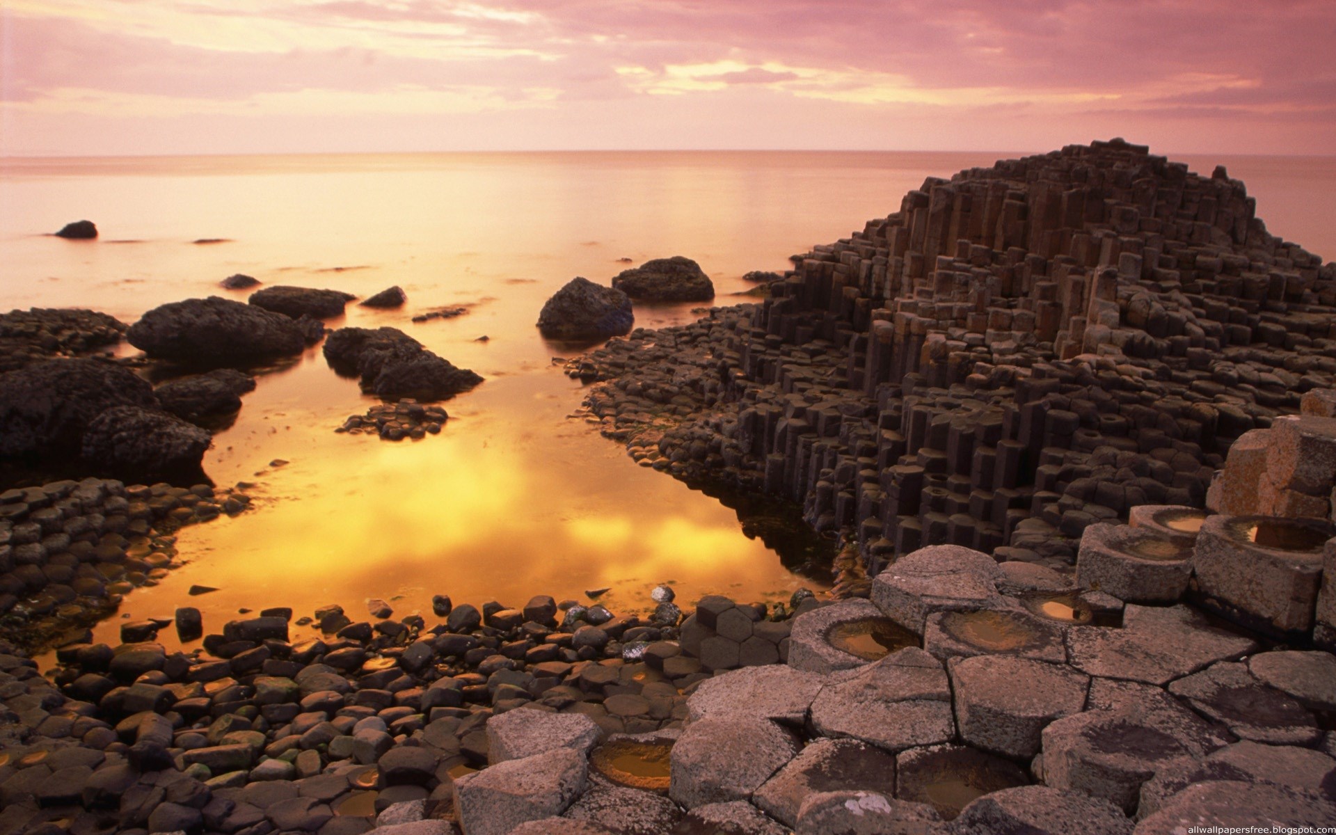 Hexagonal basalt columns on a rocky shore at sunset HD Wallpaper