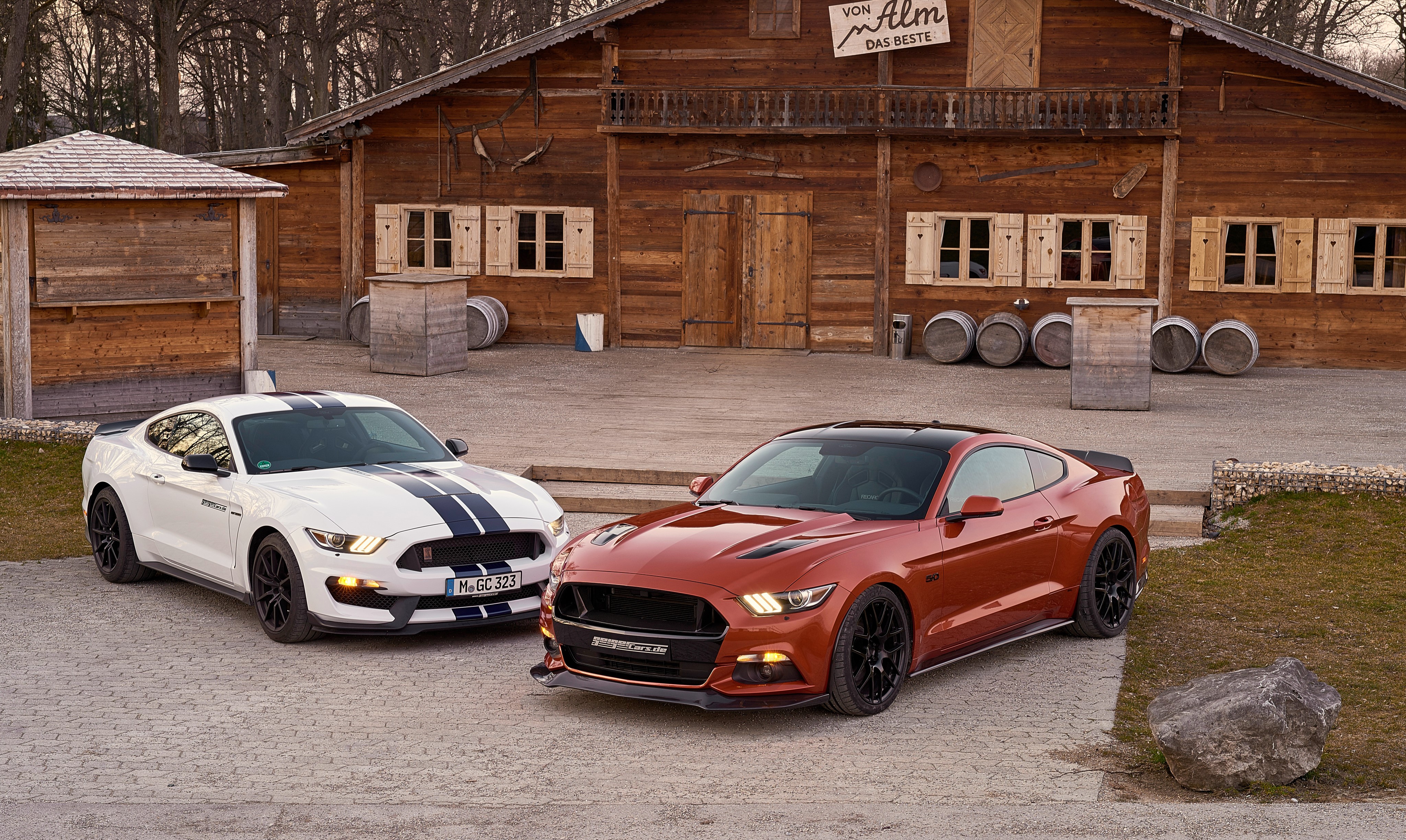 Two Ford Mustangs in front of a wooden building HD Wallpaper