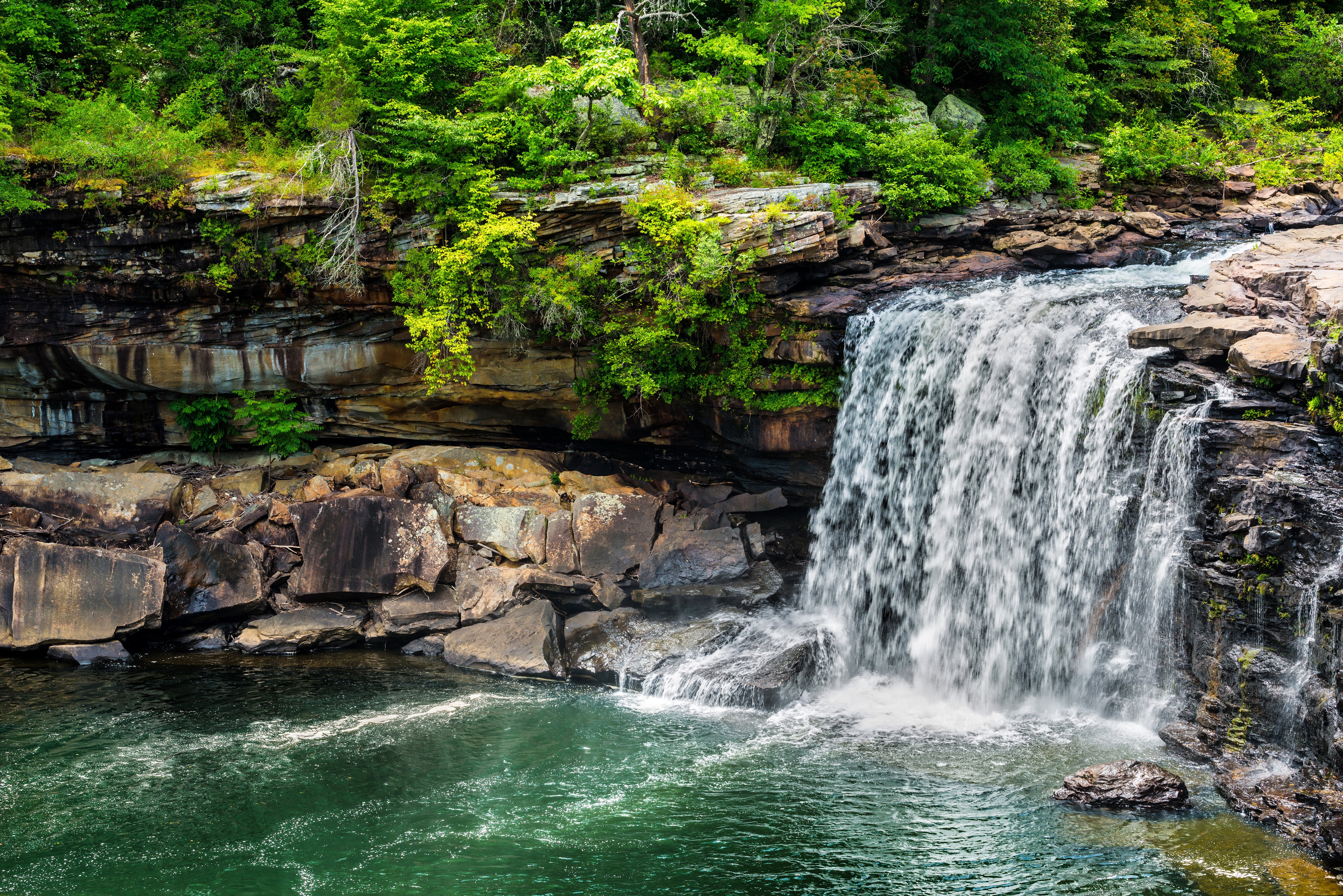 Waterfall cascading over rocks with lush green trees HD Wallpaper