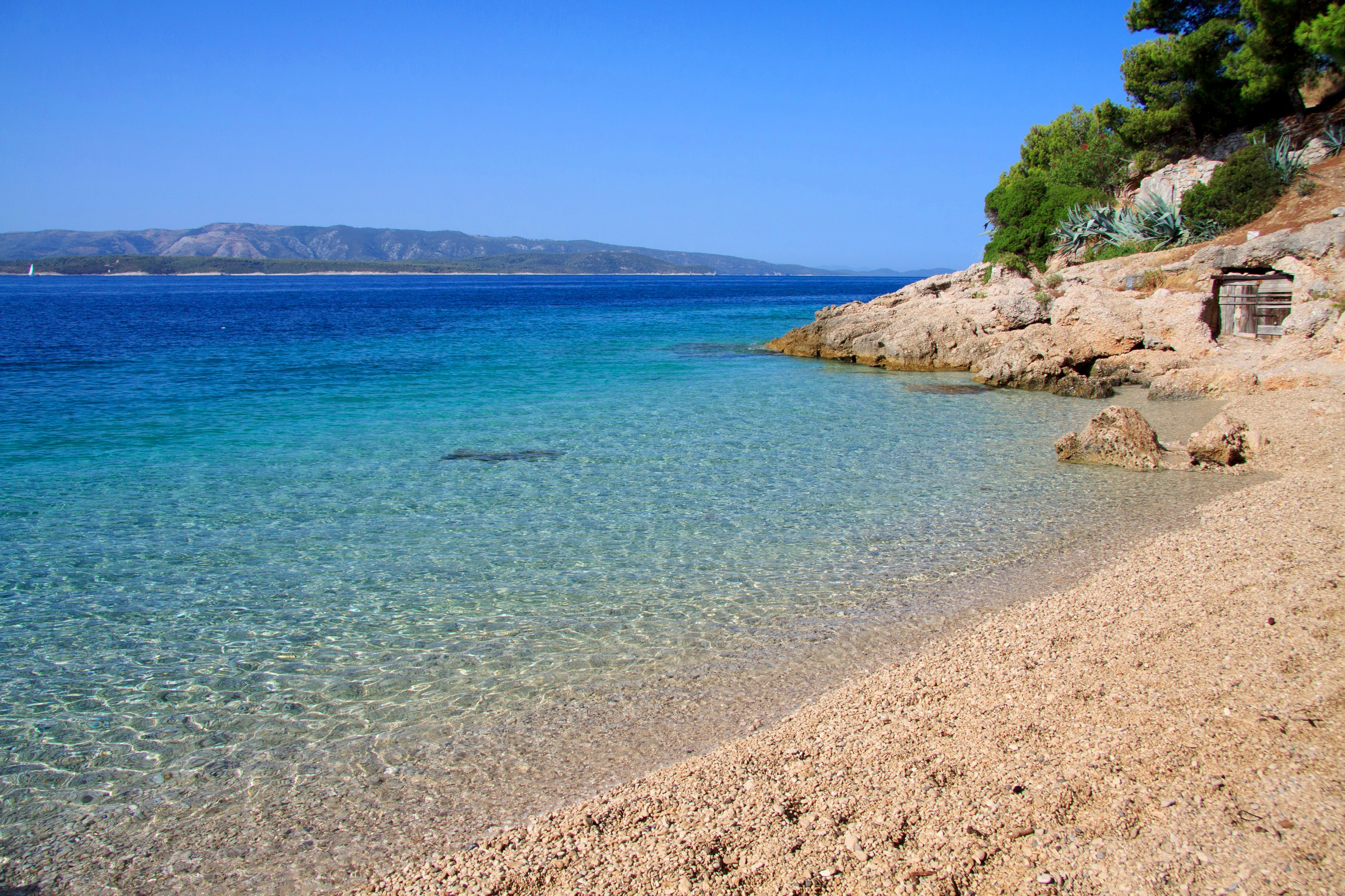 Pebble beach with clear turquoise water and rocky coast HD Wallpaper