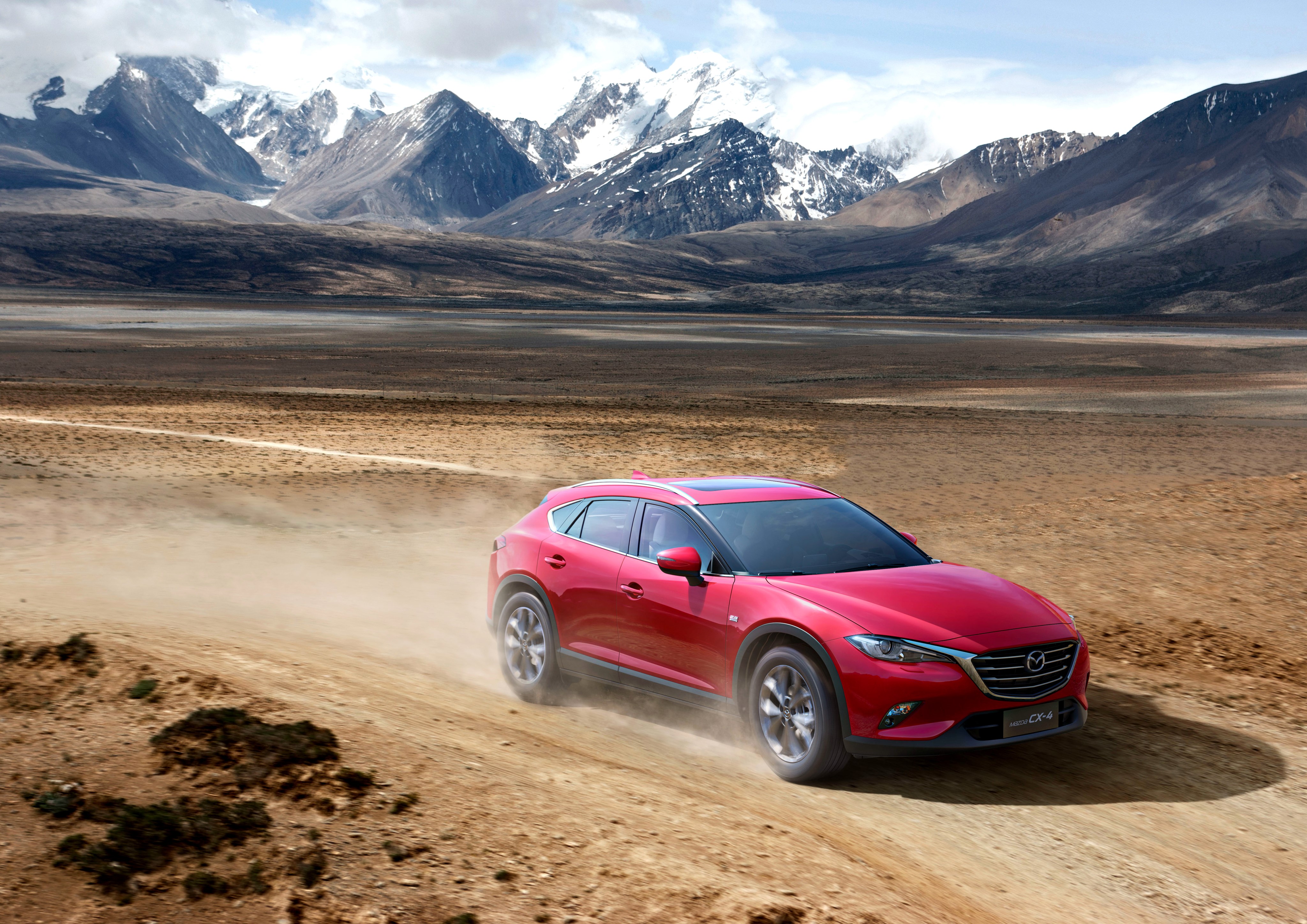 Red Mazda CX-4 driving on a dirt road with mountains HD Wallpaper