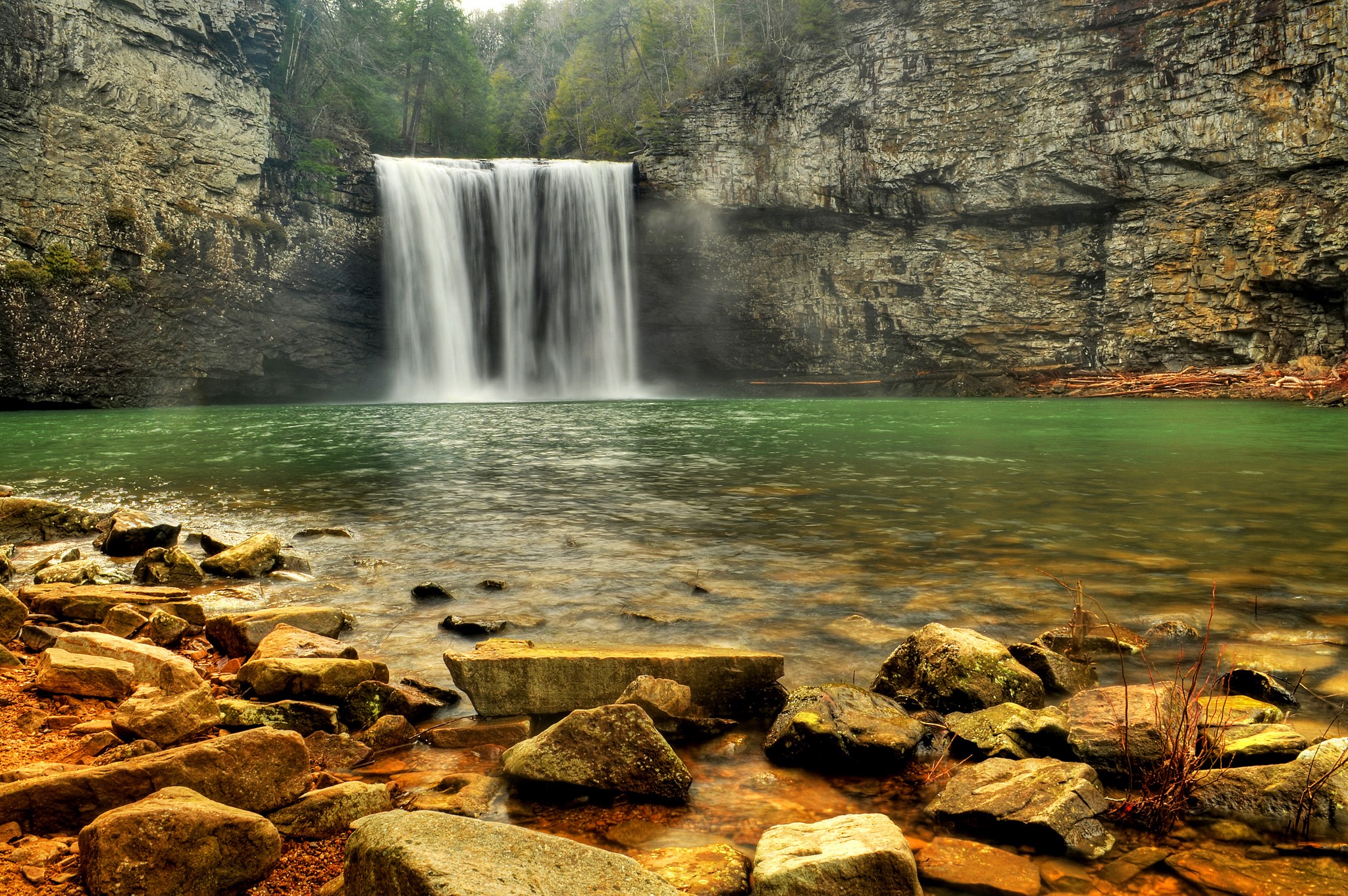 Waterfall cascading into a green pool with rocky shore HD Wallpaper