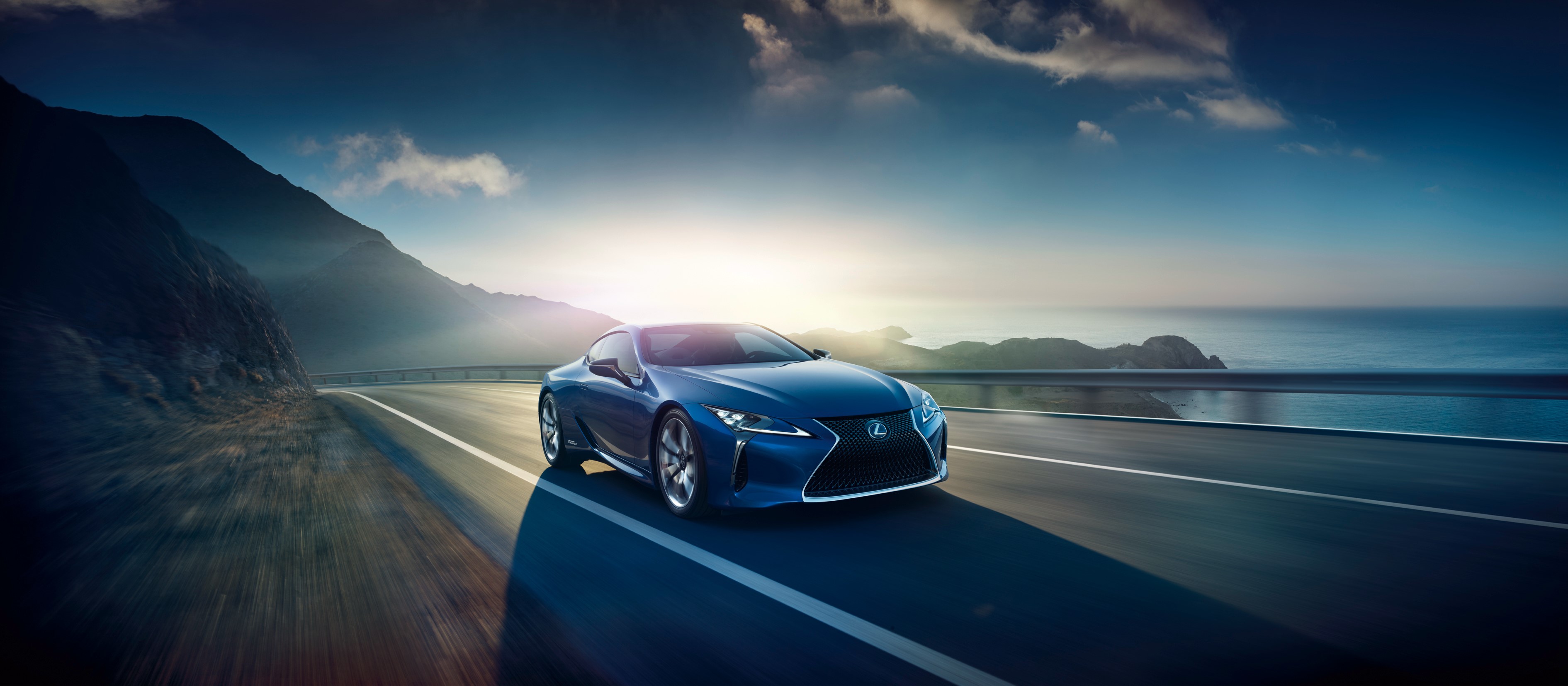 Blue Lexus LC driving on a coastal road at sunset HD Wallpaper