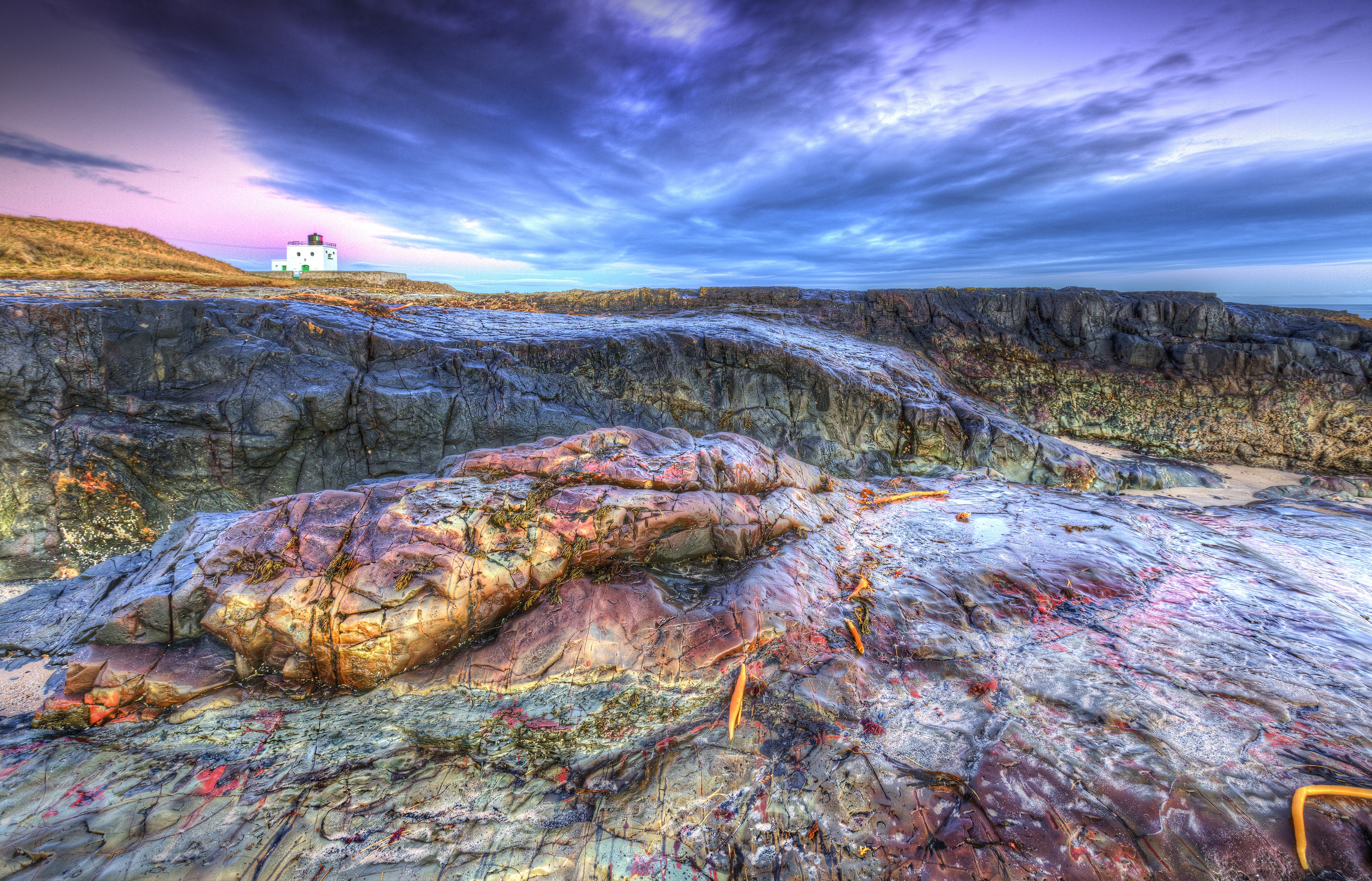 Bamburgh Beach Lighthouse on rocky coast under dramatic sky HD Wallpaper