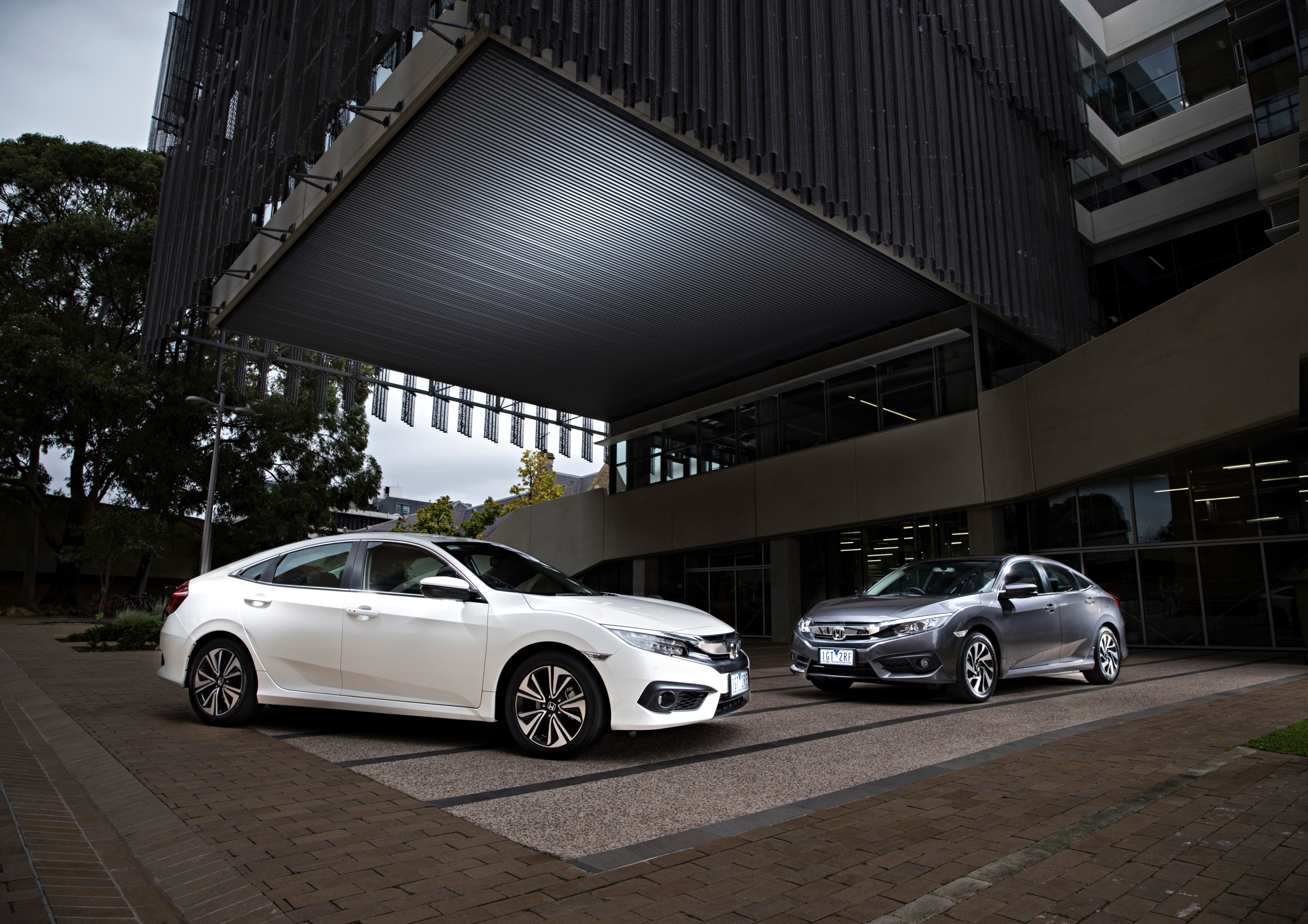 Two Honda Civic Sedans parked outside a modern building HD Wallpaper