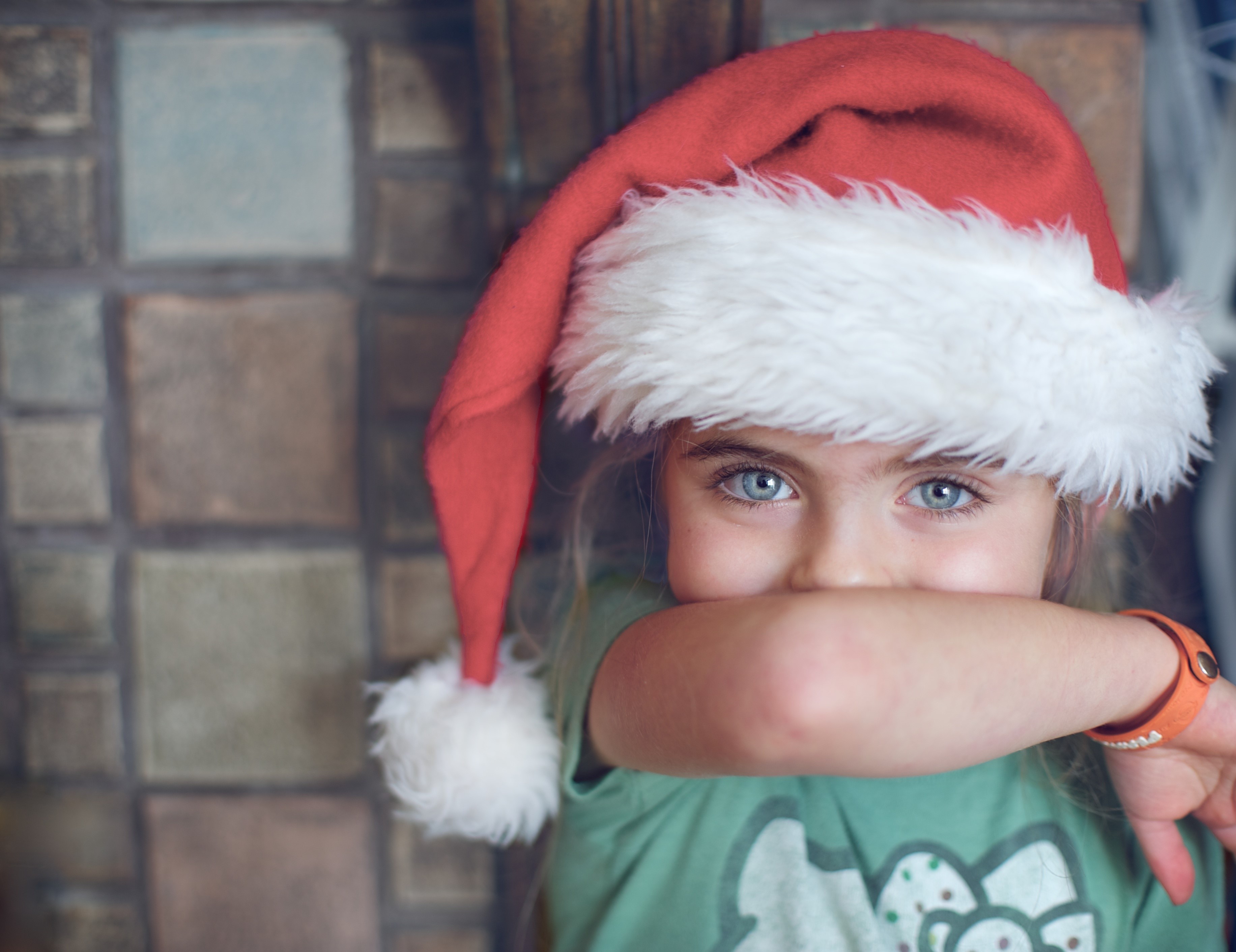 Girl wearing a Santa hat peeking over her arm HD Wallpaper