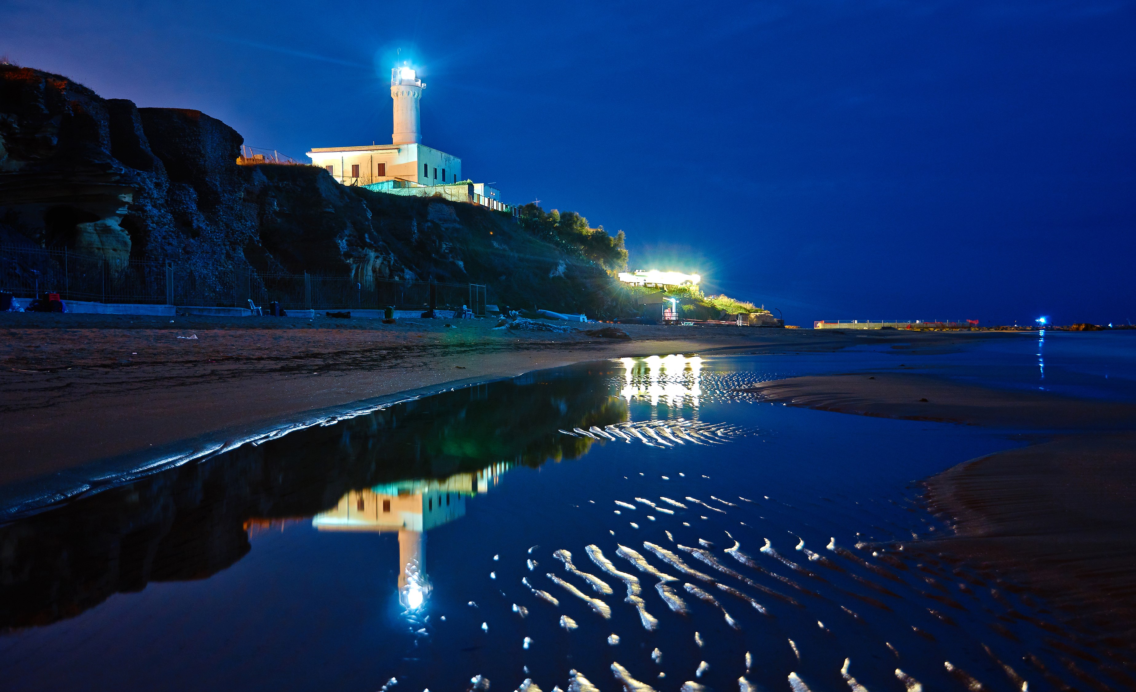 Lighthouse on cliff at night with reflection HD Wallpaper