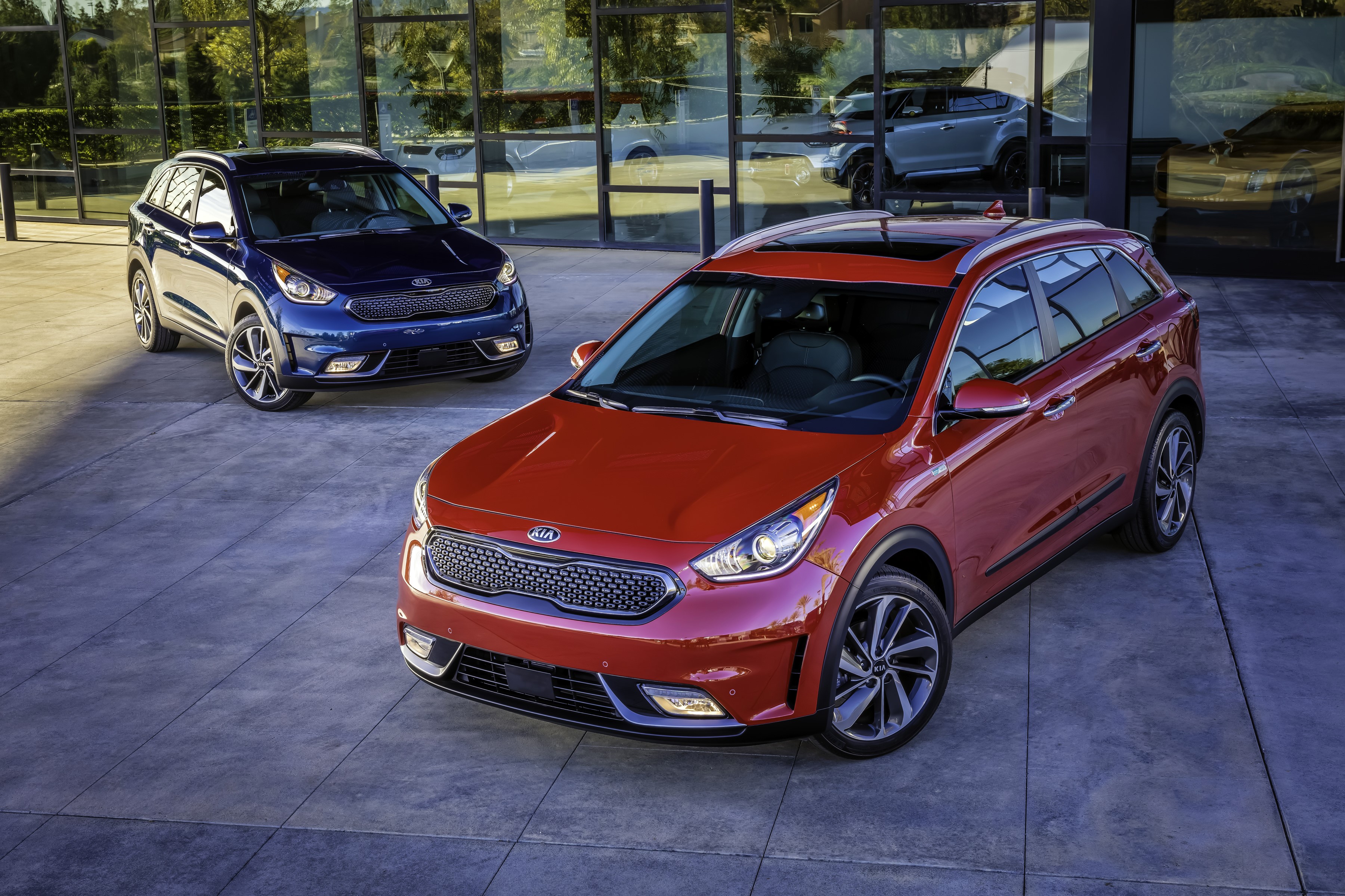 Two Kia Niro Hybrid cars parked outside a modern building HD Wallpaper