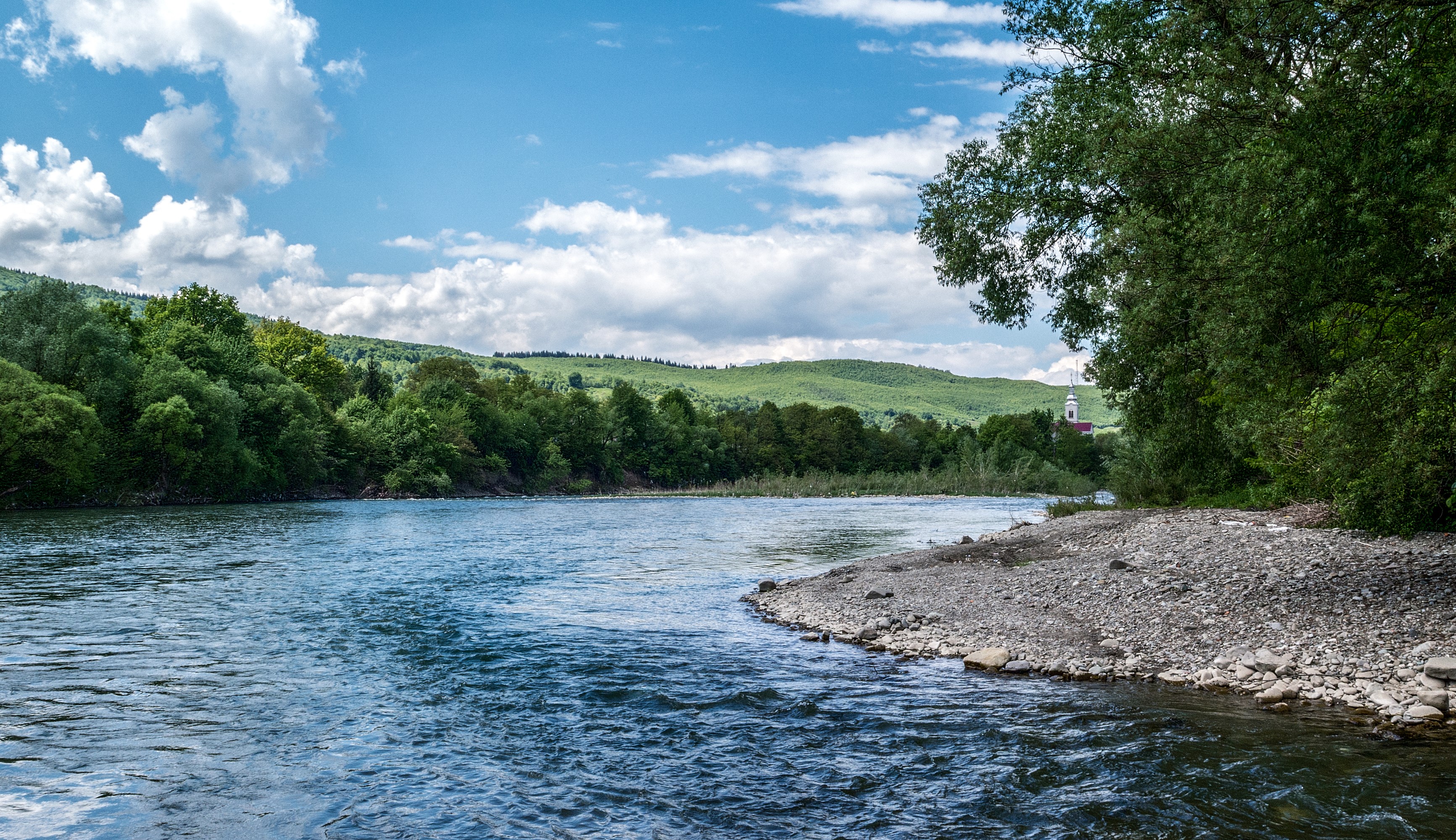 River flowing through a green landscape with hills and a church HD Wallpaper