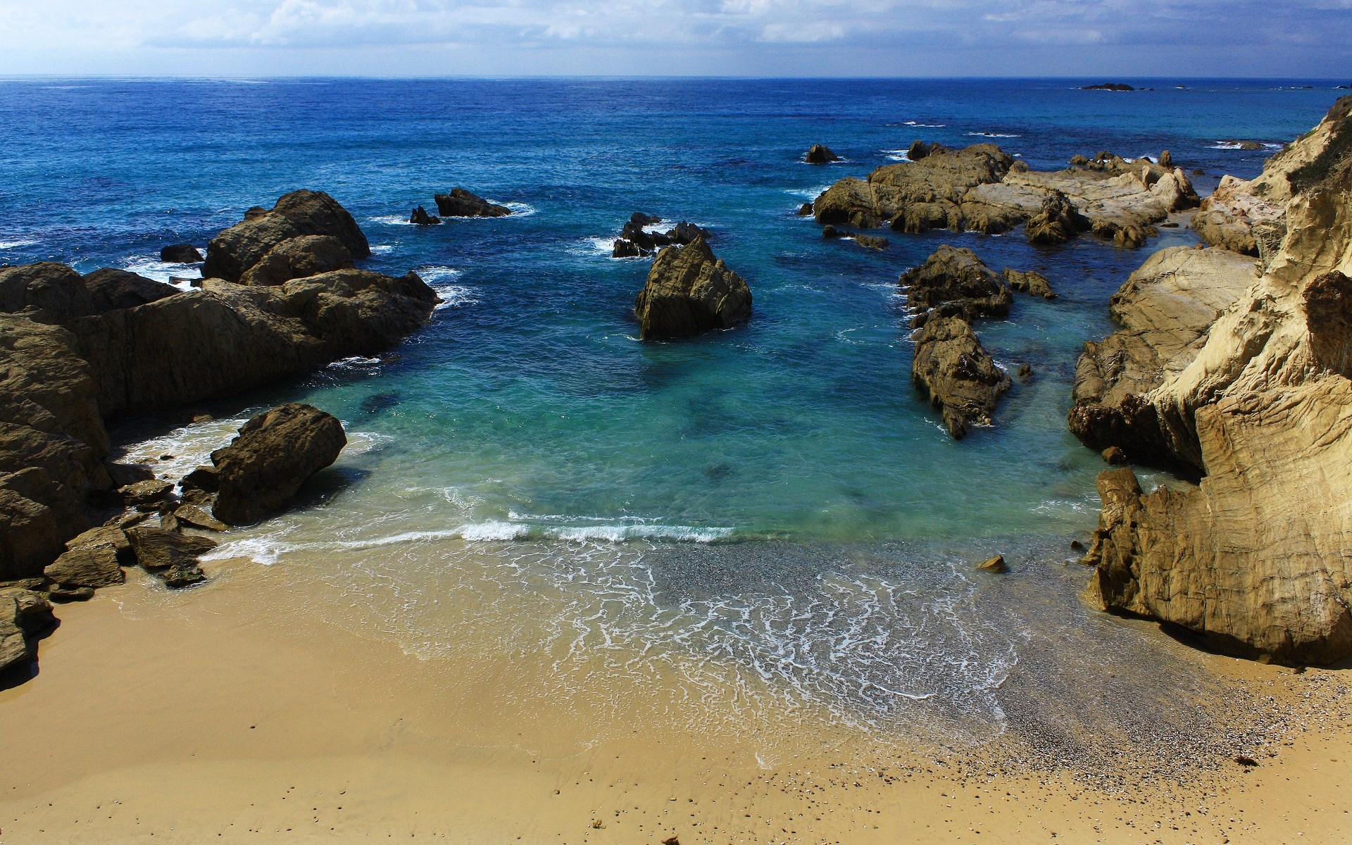 Rocky coastline with a sandy beach and blue ocean HD Wallpaper