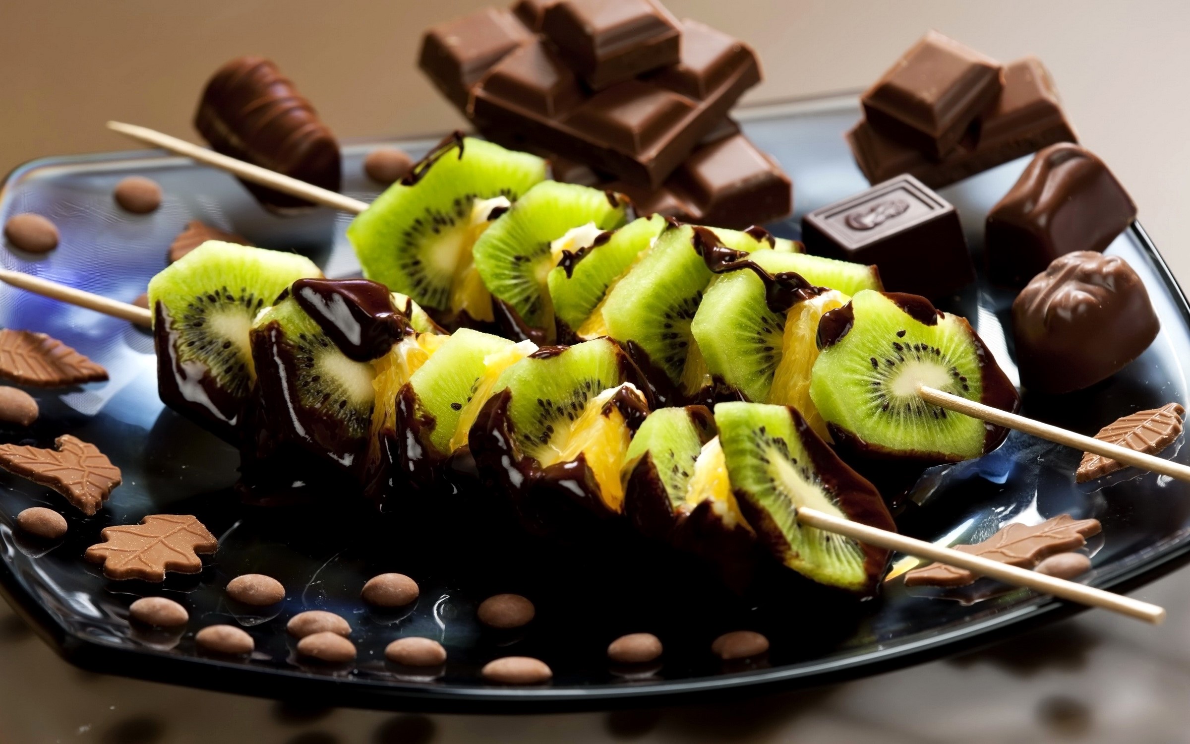 Chocolate-covered kiwi skewers with chocolates and cookies HD Wallpaper