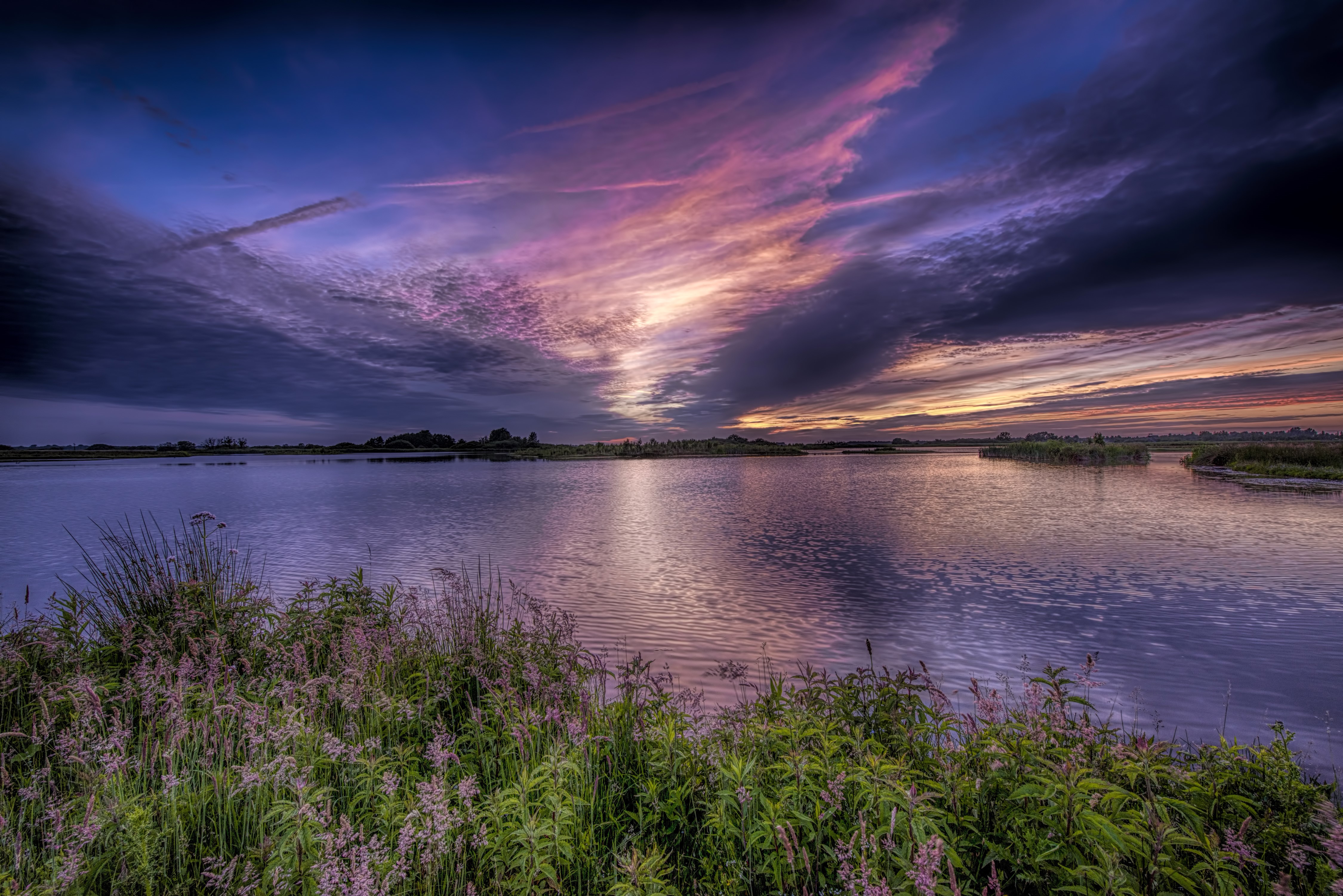 Sunset over a lake with dramatic clouds and foreground grass HD Wallpaper