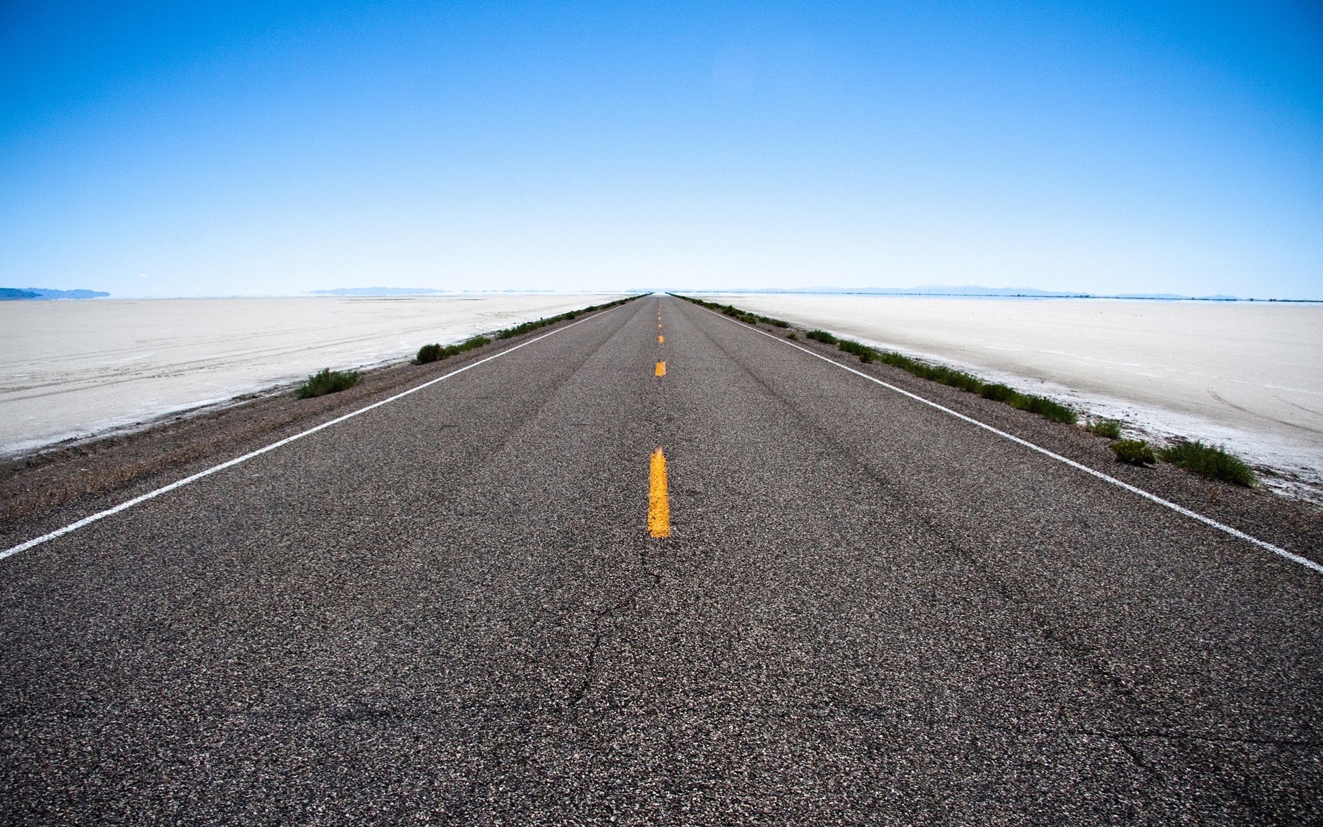 Endless road through a salt flat under a clear blue sky HD Wallpaper