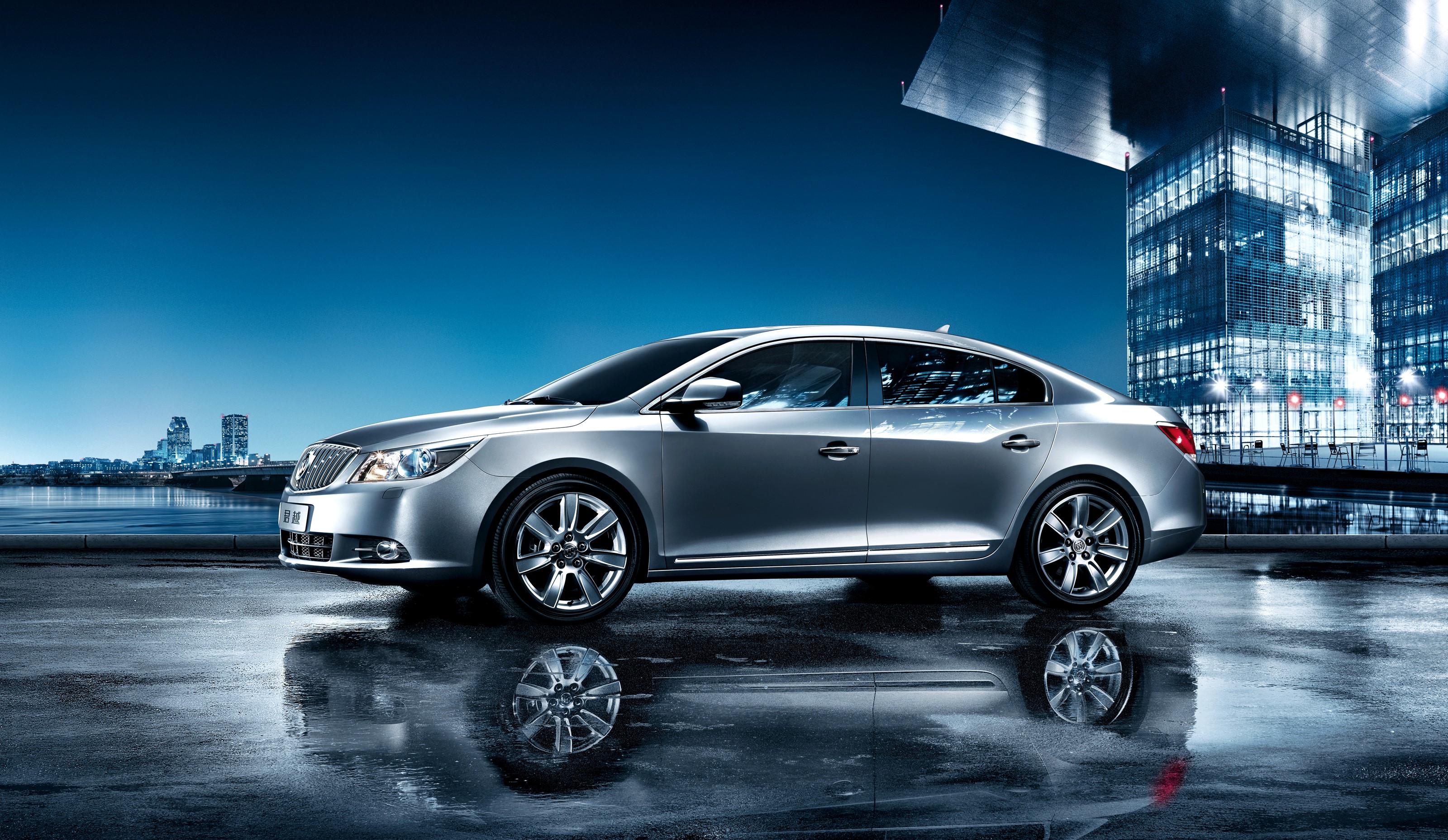 Silver Buick LaCrosse parked by a city skyline at night HD Wallpaper