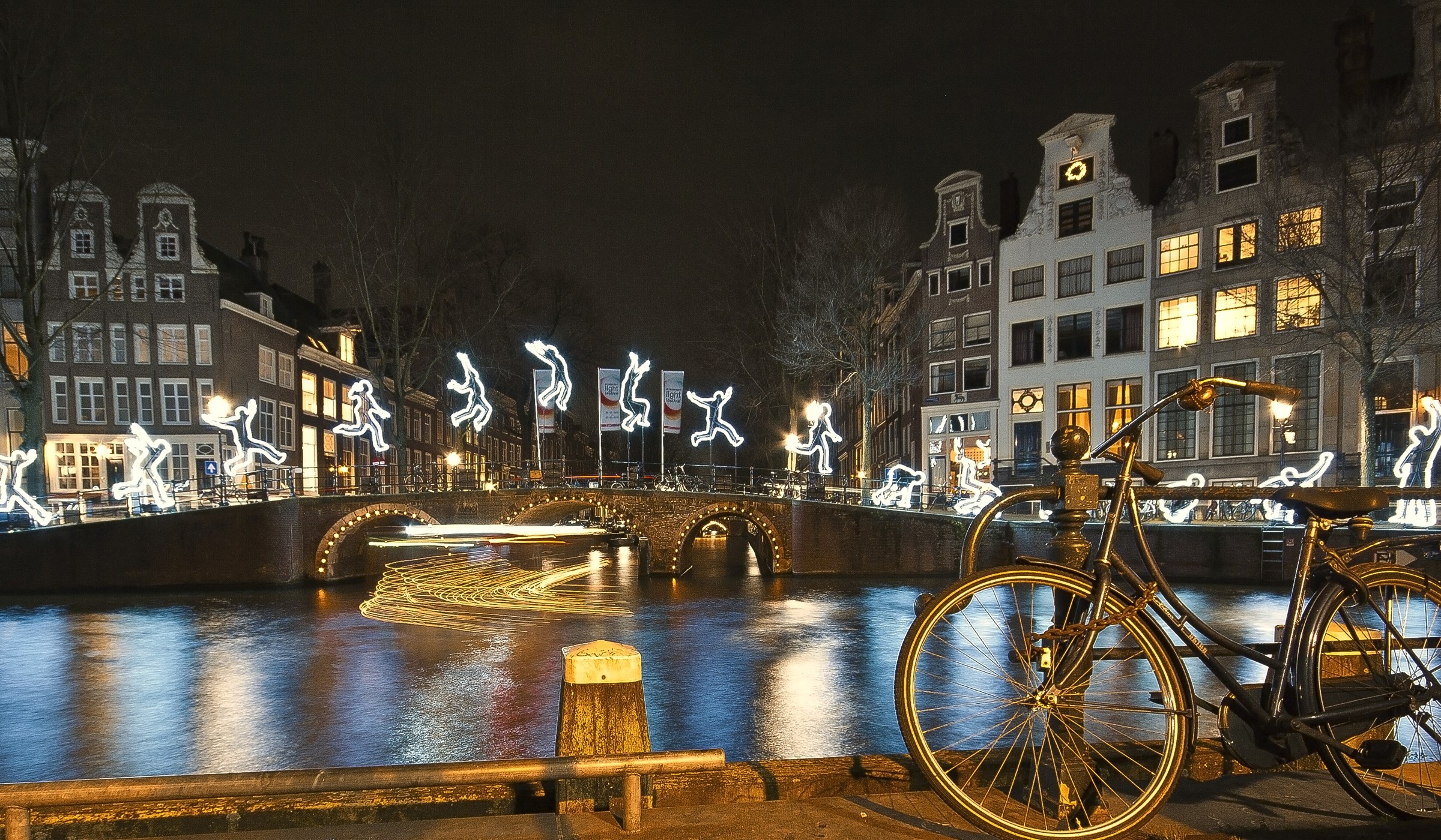 Amsterdam canal at night with illuminated figures and bicycle HD Wallpaper