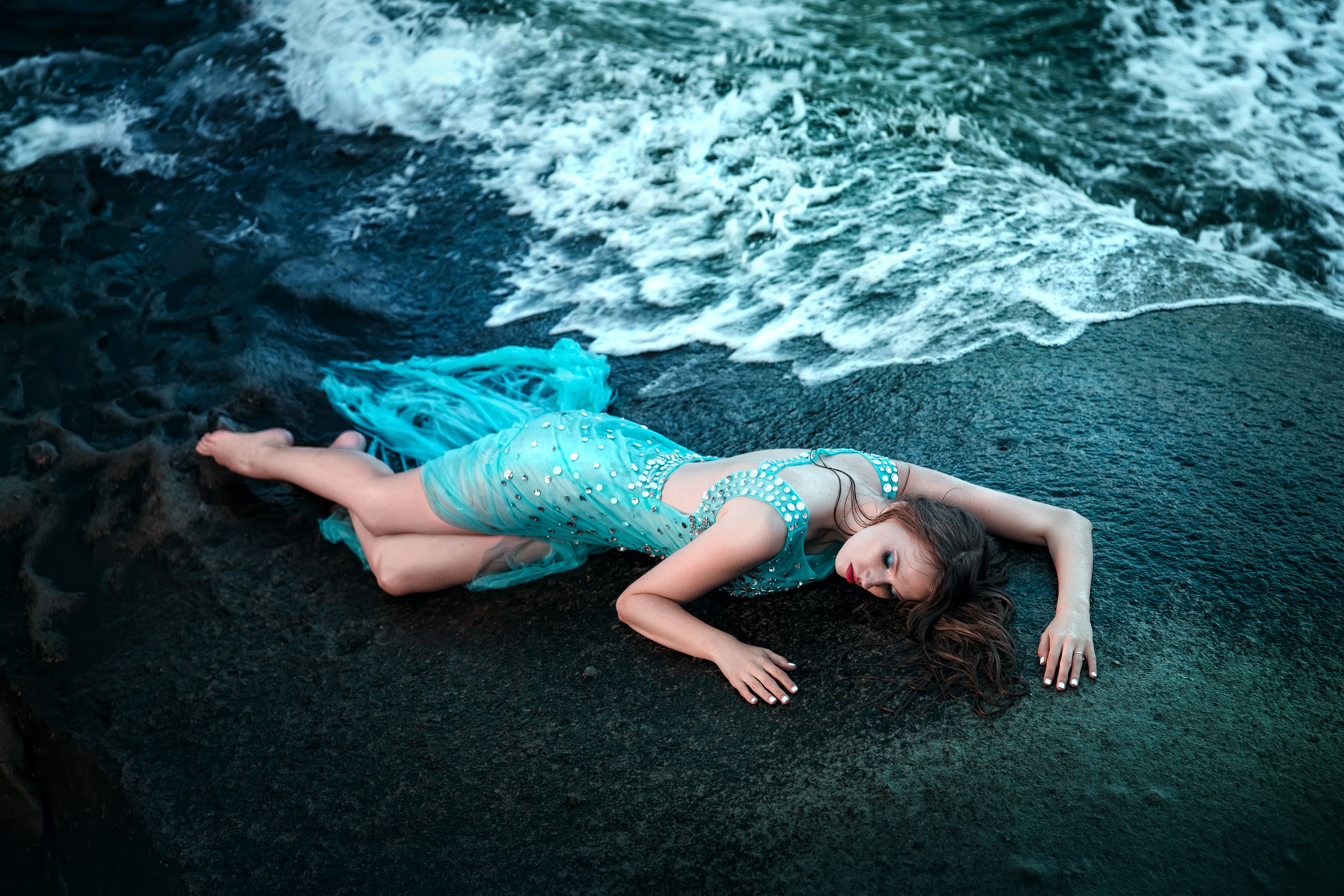 Woman in a blue dress lying on a dark shore with waves HD Wallpaper