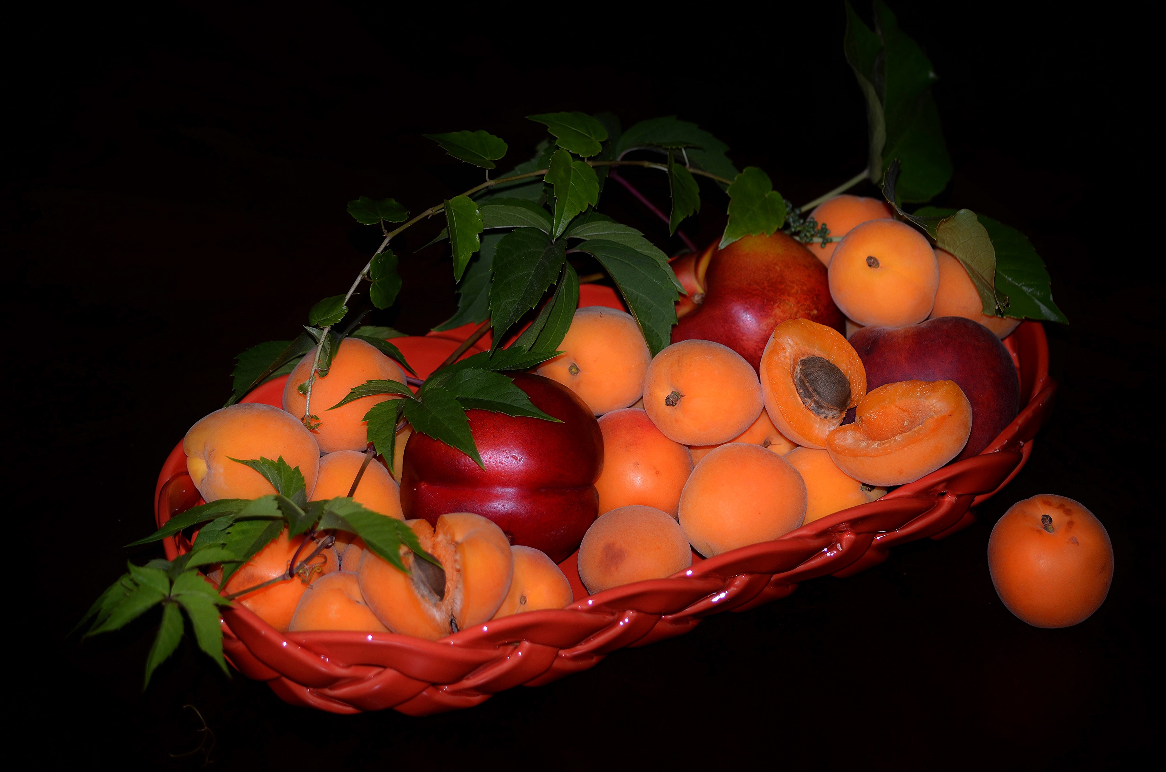 Apricots and nectarines in a red basket with foliage HD Wallpaper
