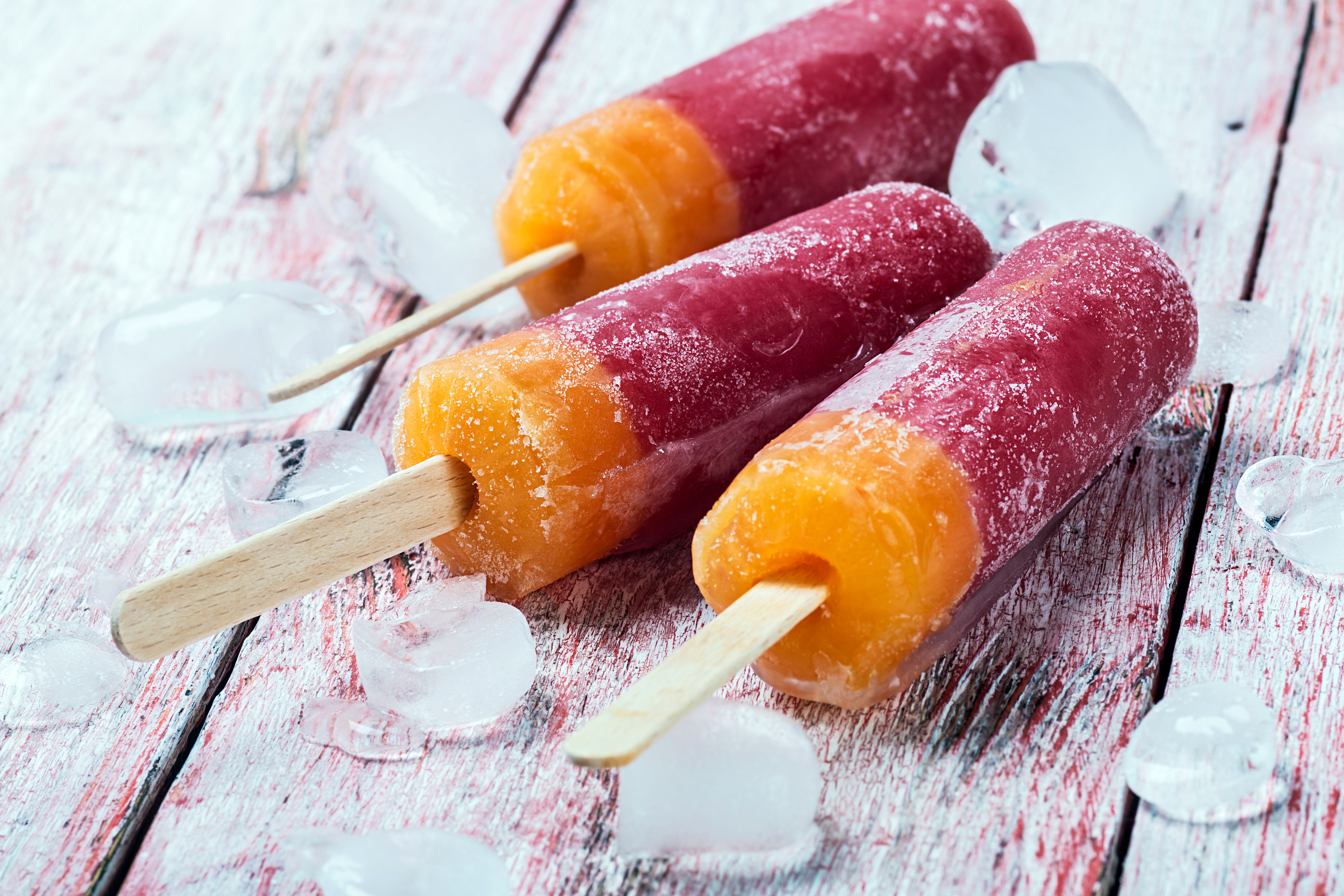 Three two-toned popsicles with ice on a wooden surface HD Wallpaper