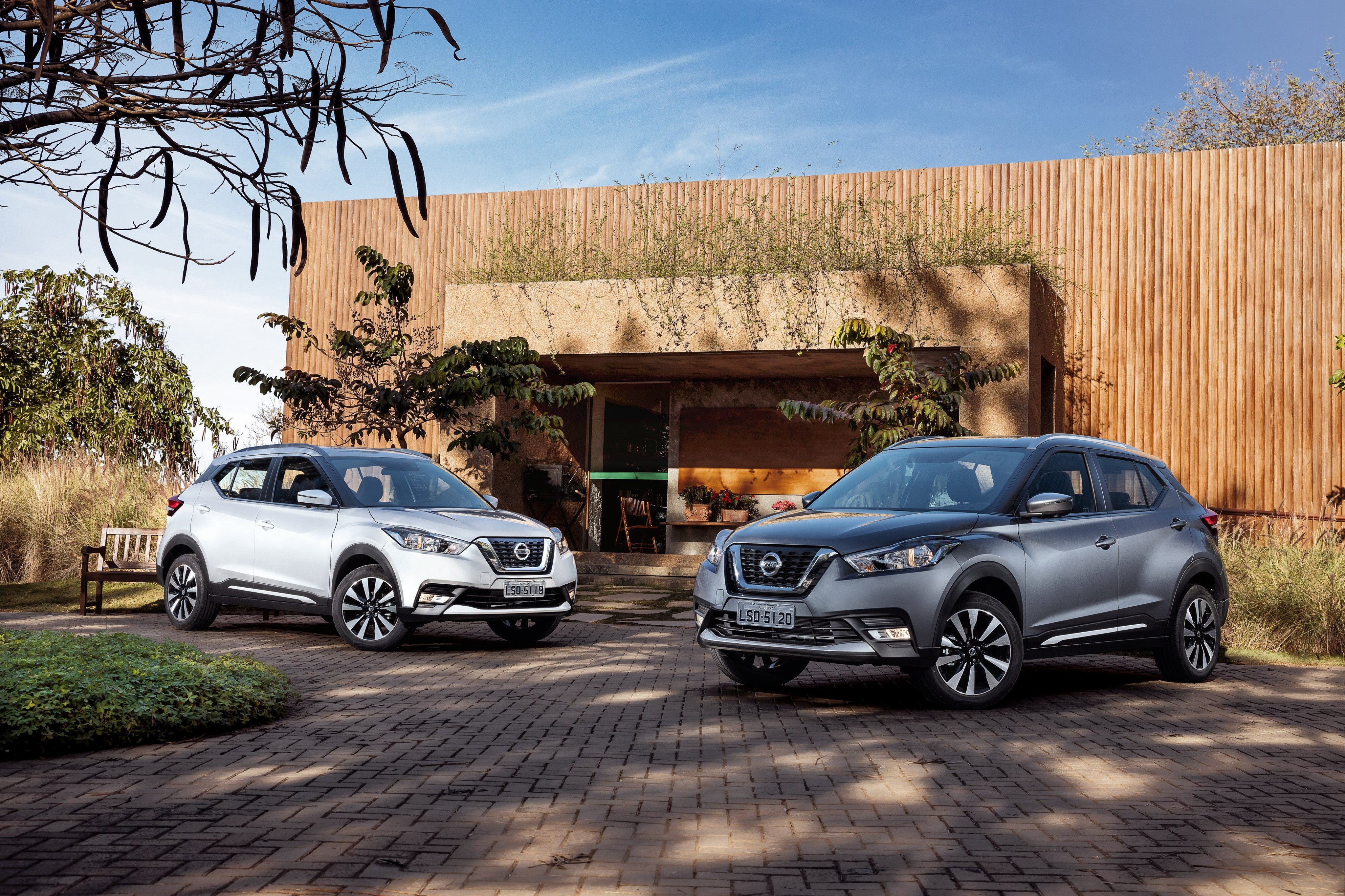 Two Nissan Kicks cars parked outside a modern building HD Wallpaper