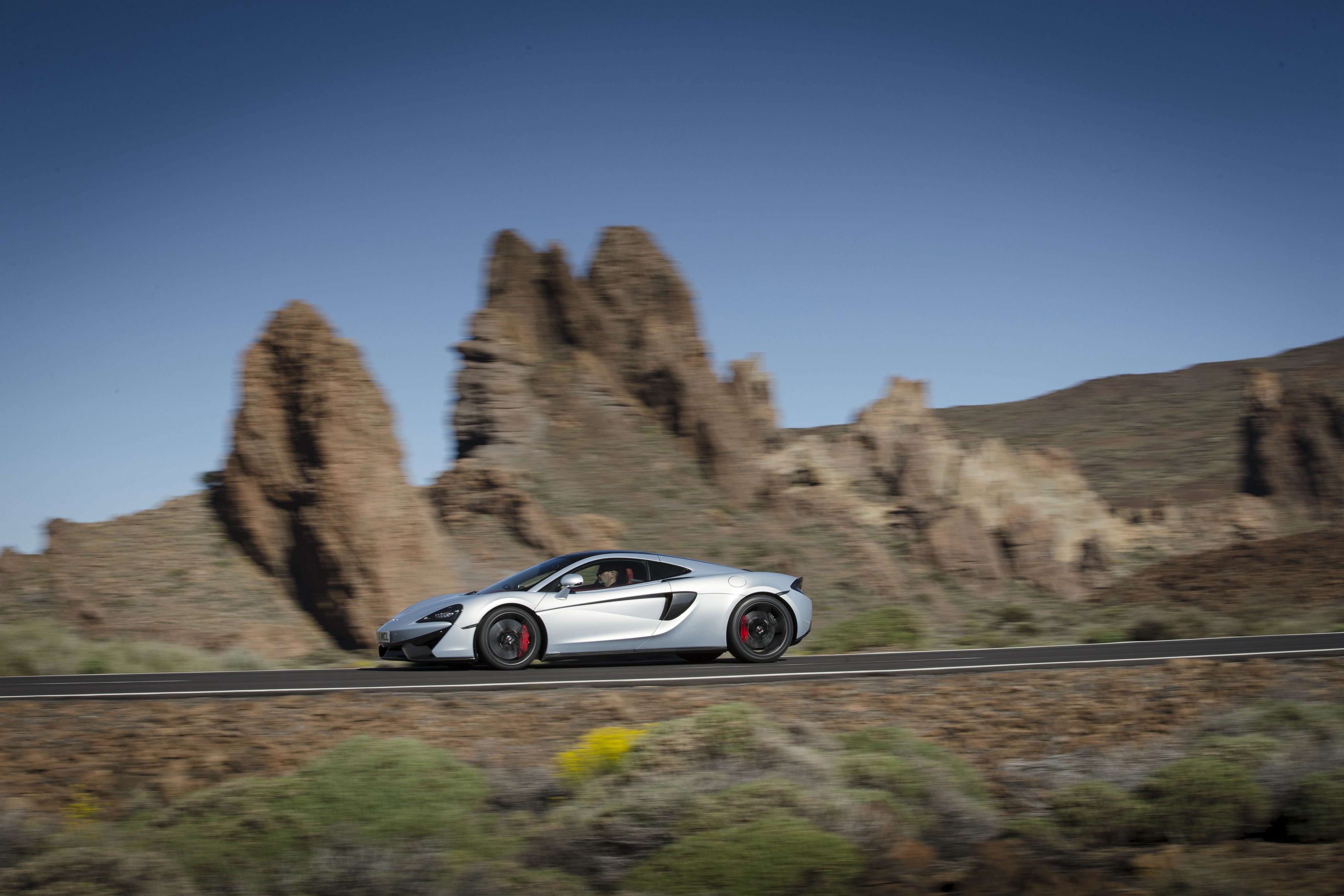 McLaren 570GT driving on a road HD Wallpaper