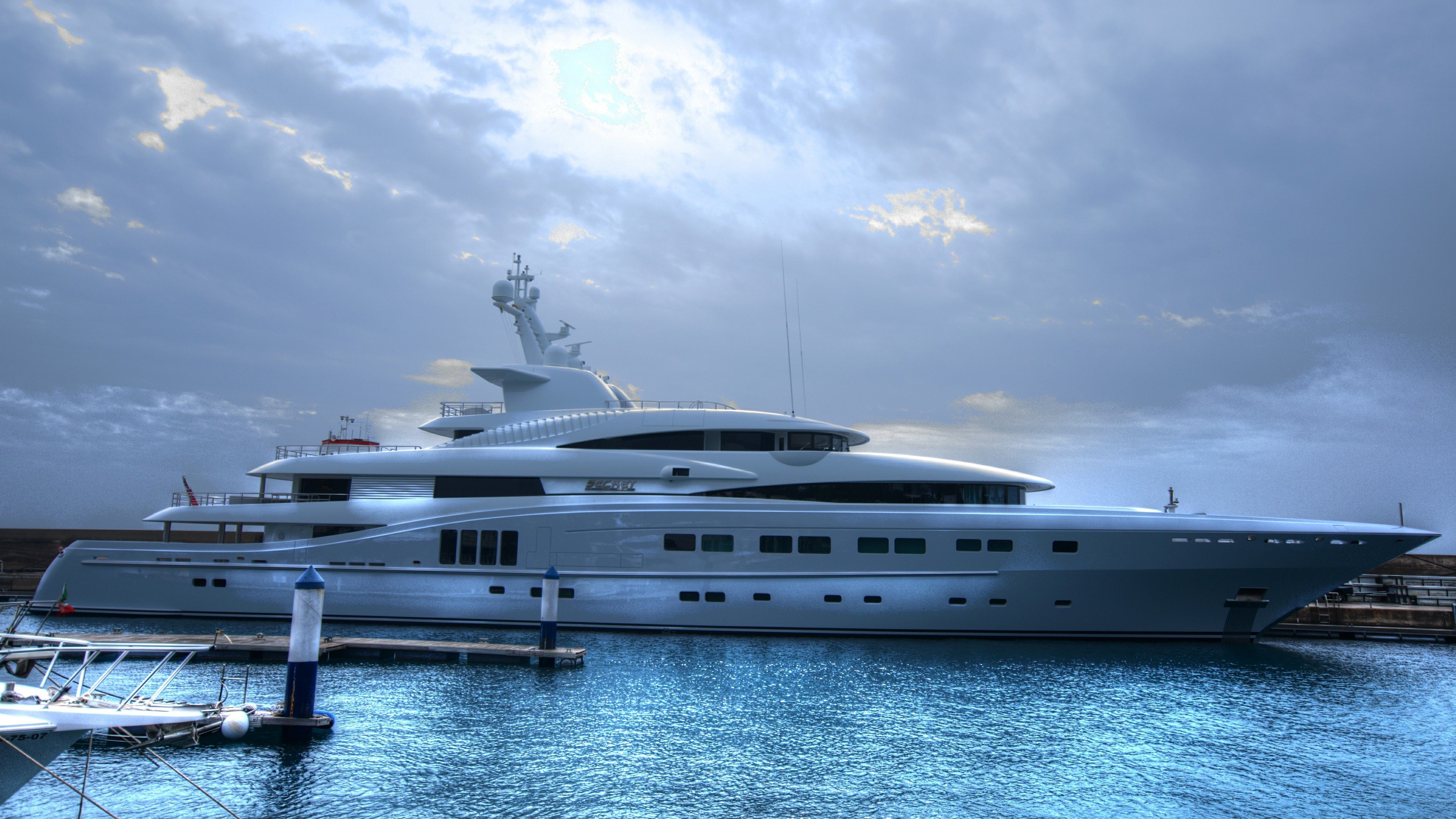 Luxury yacht docked in a harbor under a cloudy sky HD Wallpaper