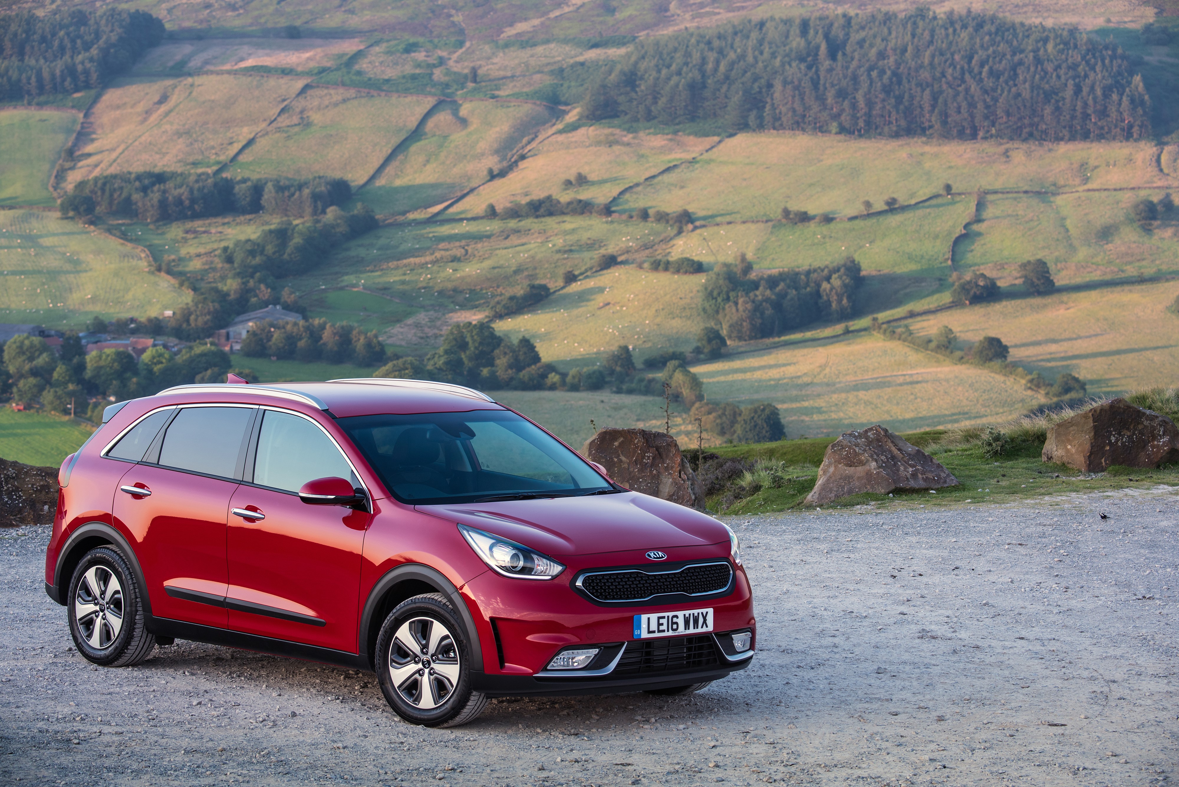 Red 2016 Kia Niro parked on gravel with rolling hills background HD Wallpaper
