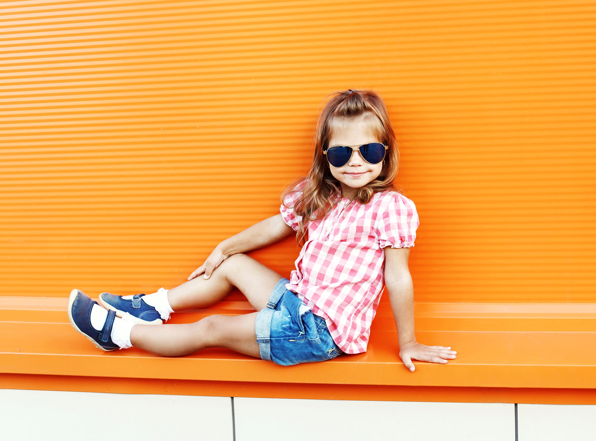 Girl in sunglasses sitting against an orange wall HD Wallpaper