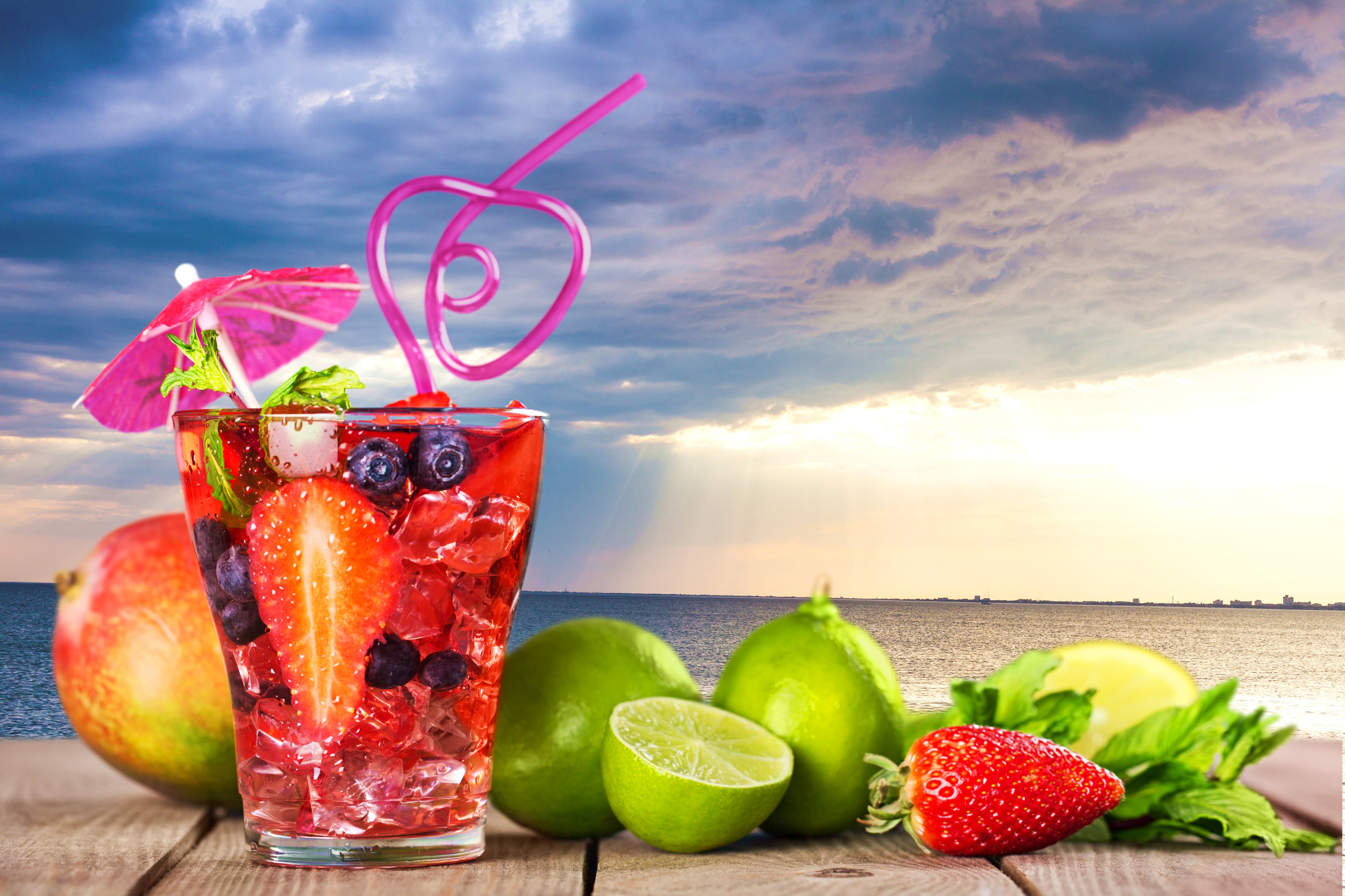 Fruit cocktail with strawberry, lime, and mango on a beach HD Wallpaper